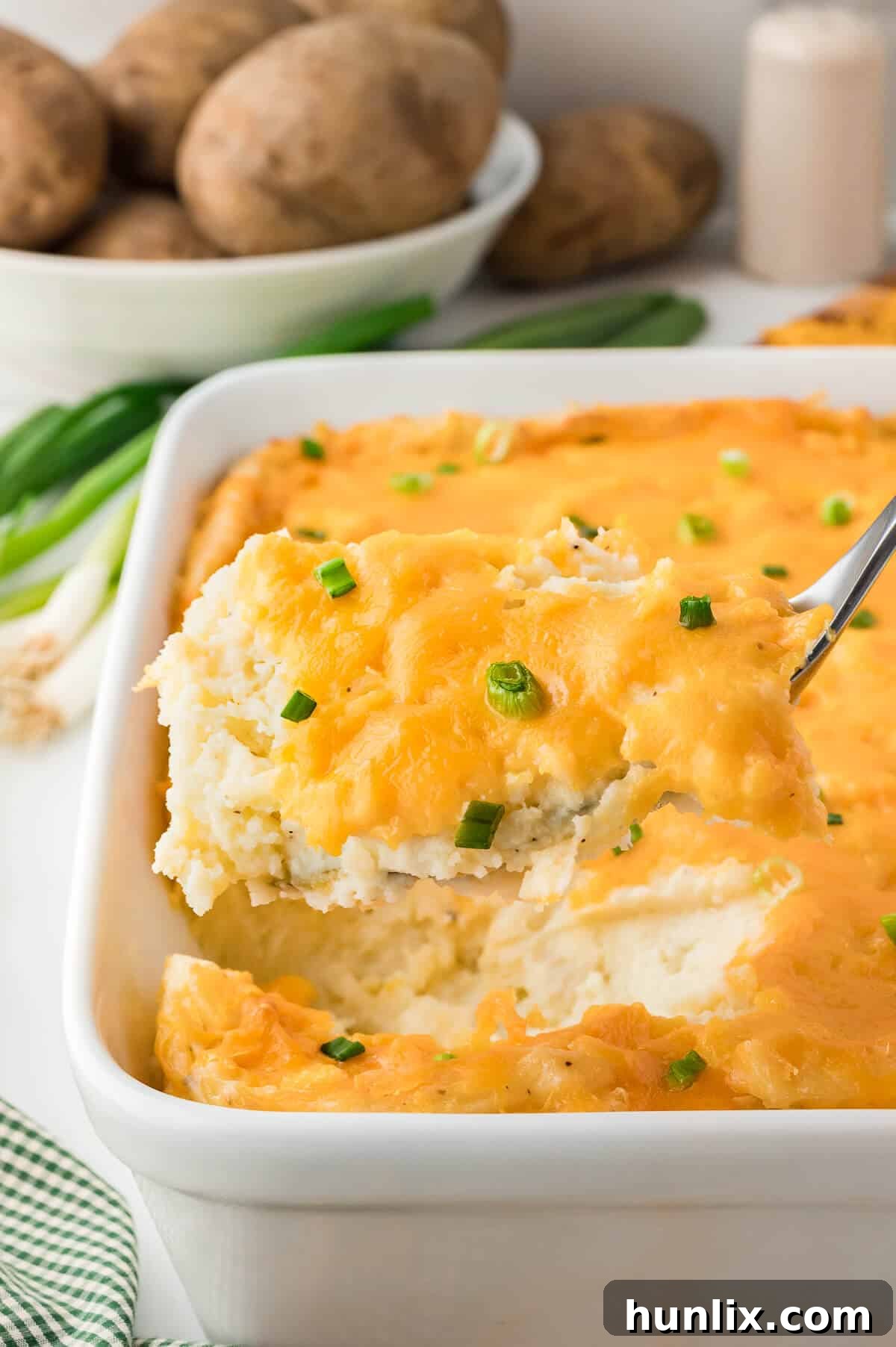A serving spoon lifting a portion of mashed potato casserole from the dish.