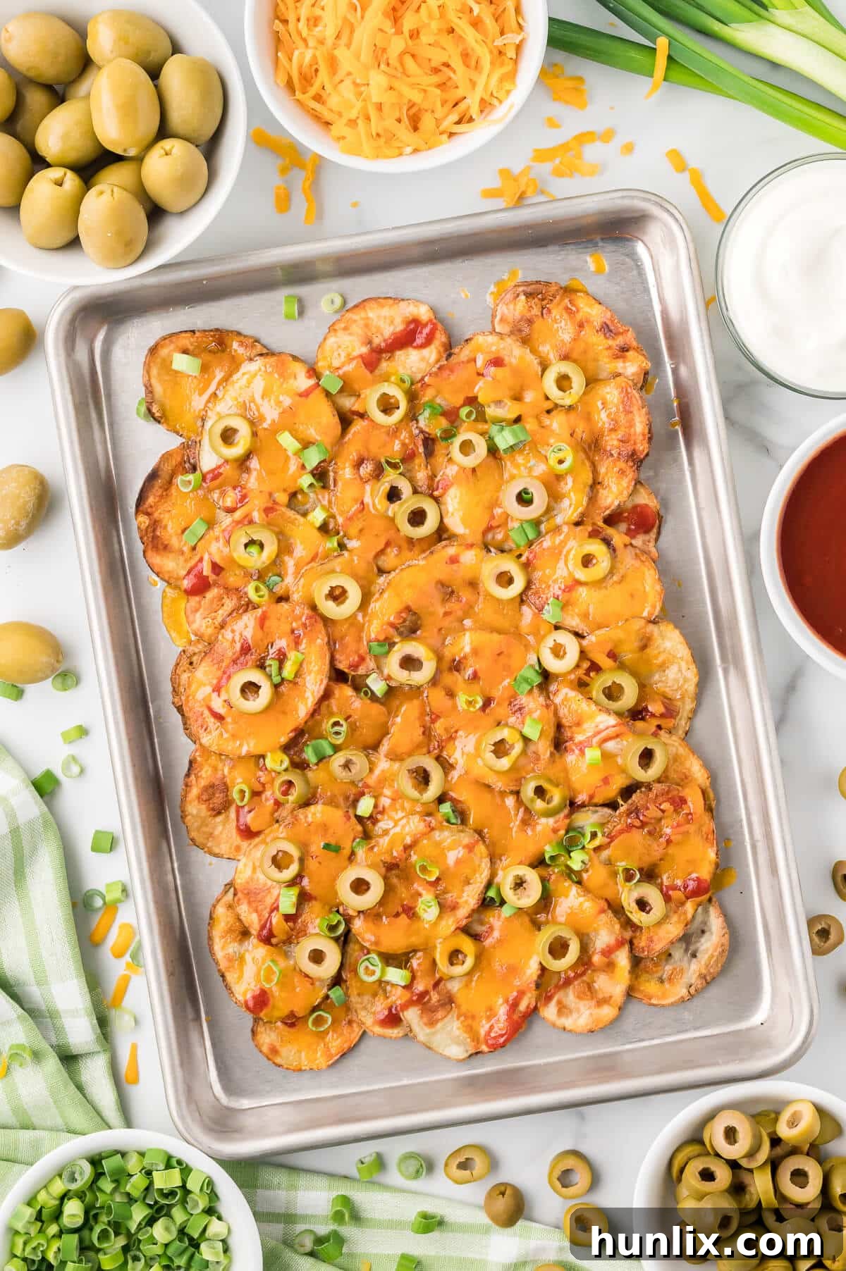Loaded Potato Nachos 2 Crispy potato nachos on a baking pan, topped with cheese, olives, and green onions.