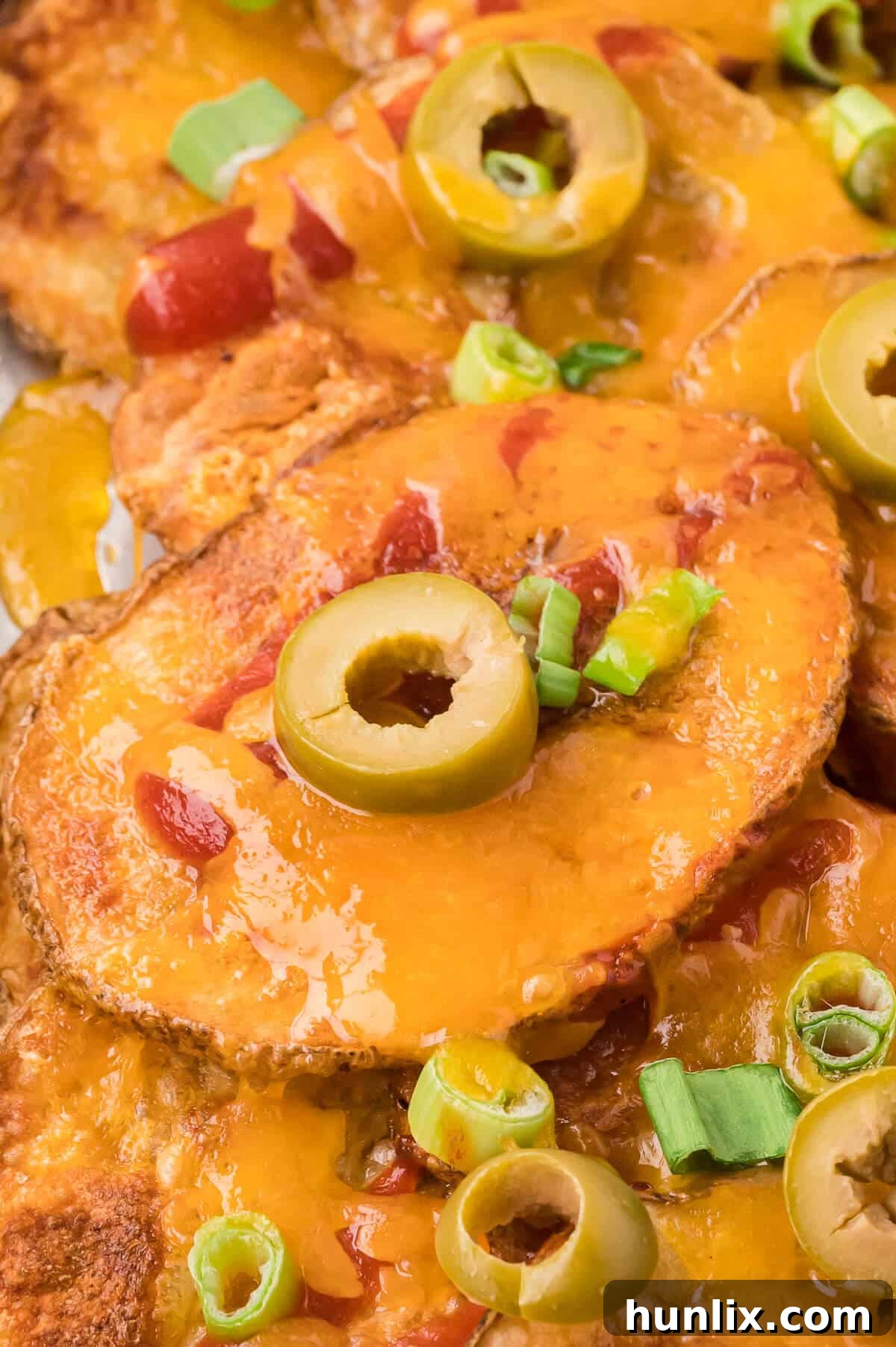 Loaded Potato Nachos 7 A close-up shot of crispy potato nachos with melted cheese, green olives, and green onions.