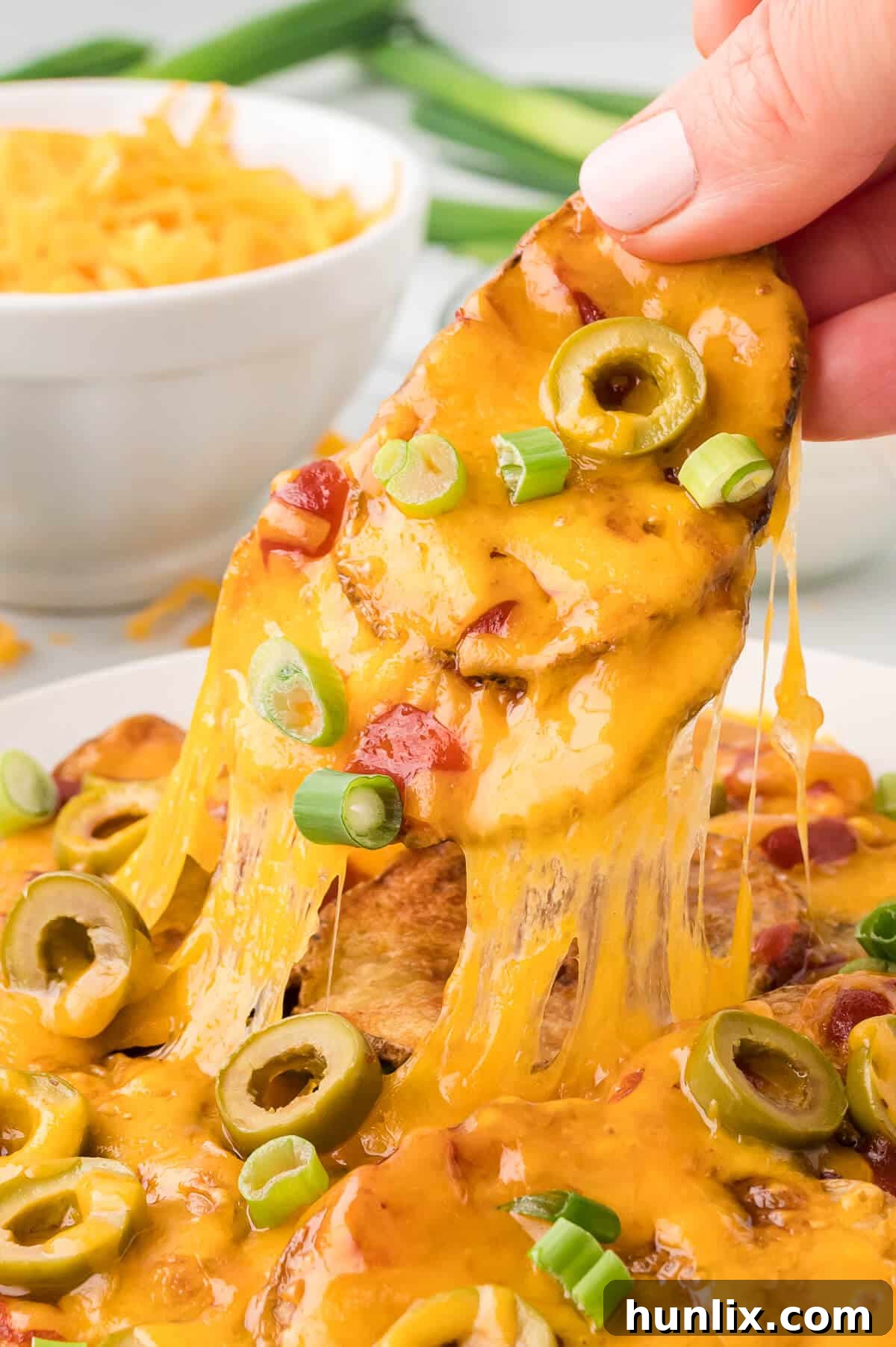 Loaded Potato Nachos 8 A hand lifting a single potato nacho off a plate, showing the melted cheese and toppings.