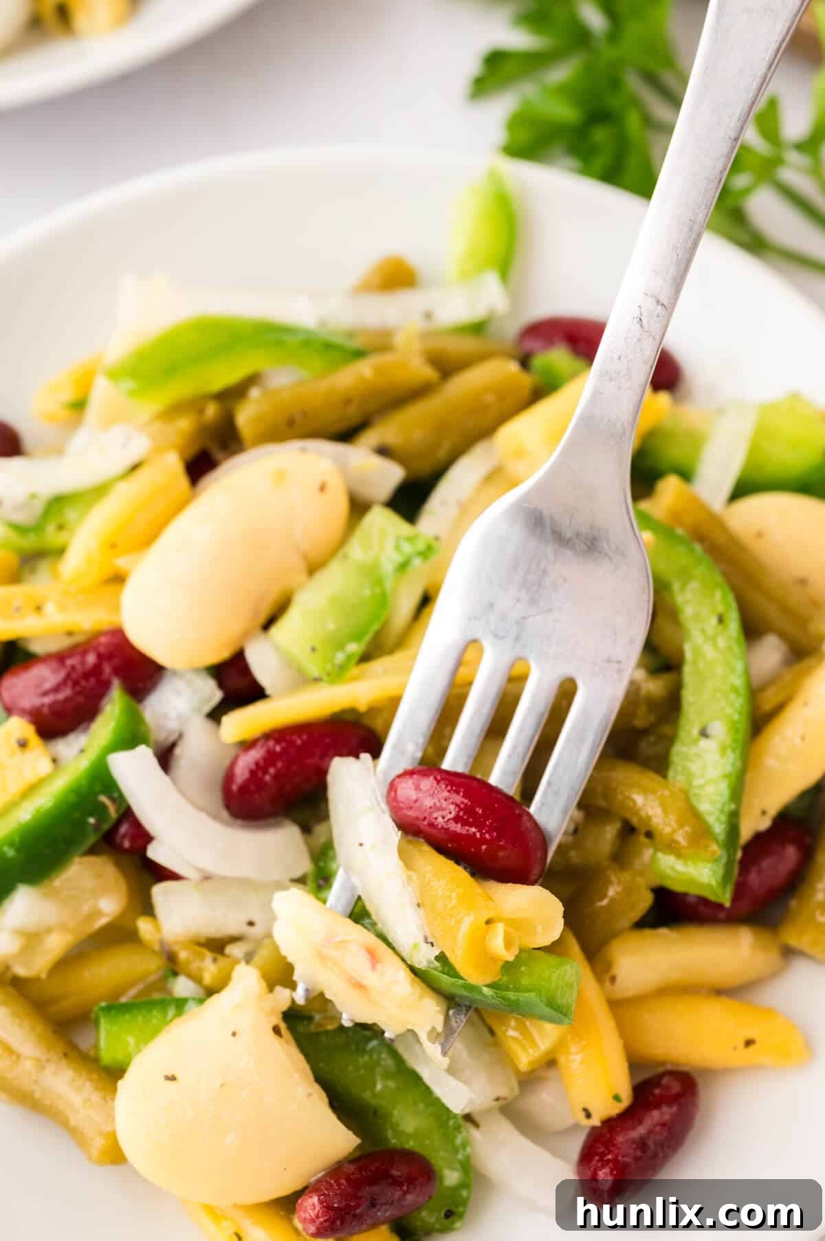 Vibrant Bean Medley 8 A close-up shot of the bean salad on a white plate with a fork, emphasizing its appetizing texture, colorful fresh ingredients, and readiness for eating.