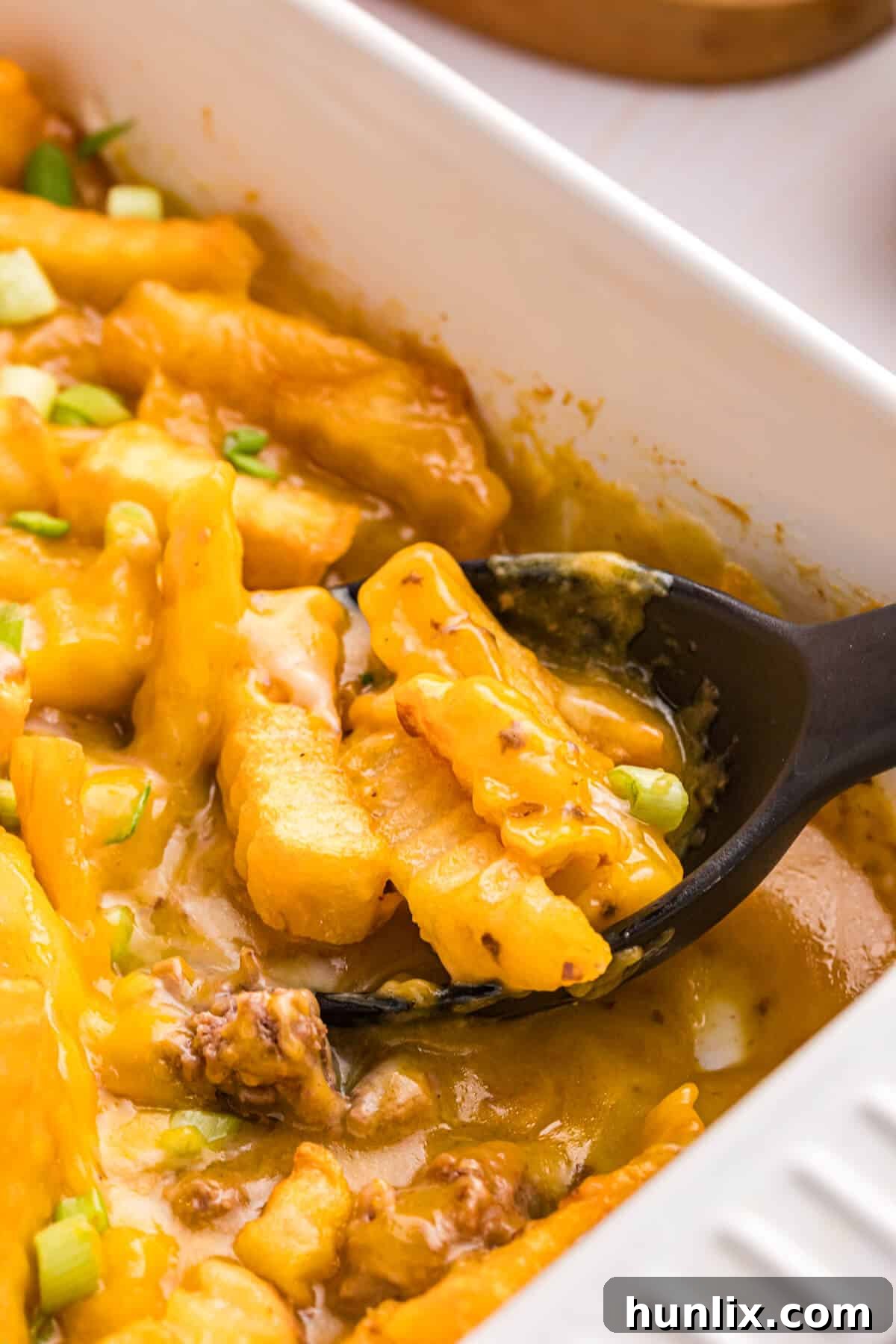 Crispy Spud Bake 5 A close-up of French Fry Casserole in the pan with a serving spoon, highlighting the crispy golden fries and creamy interior, ready for serving.
