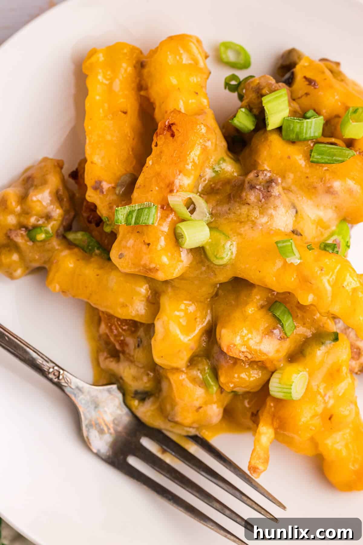 Crispy Spud Bake 7 A fork taking a bite from a plate of French Fry Casserole, showing the layers of crispy fries, creamy sauce, and seasoned meat.