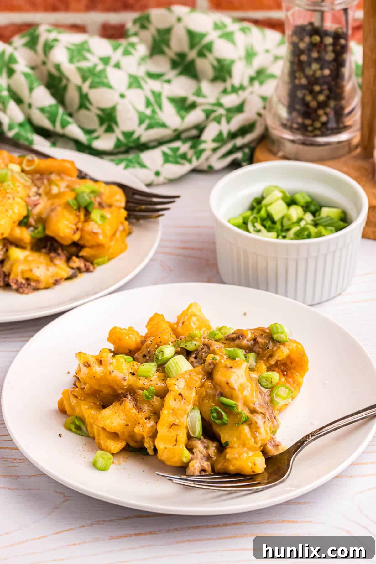 Crispy Spud Bake 8 A close-up of a generous serving of French Fry Casserole on a plate with a fork, emphasizing its hearty and comforting appeal.
