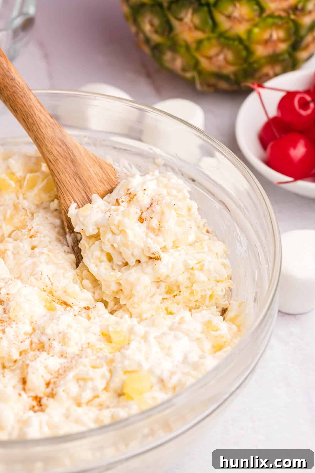 A beautifully presented bowl of creamy pineapple rice pudding, garnished and ready to serve, with a wooden spoon resting in it.