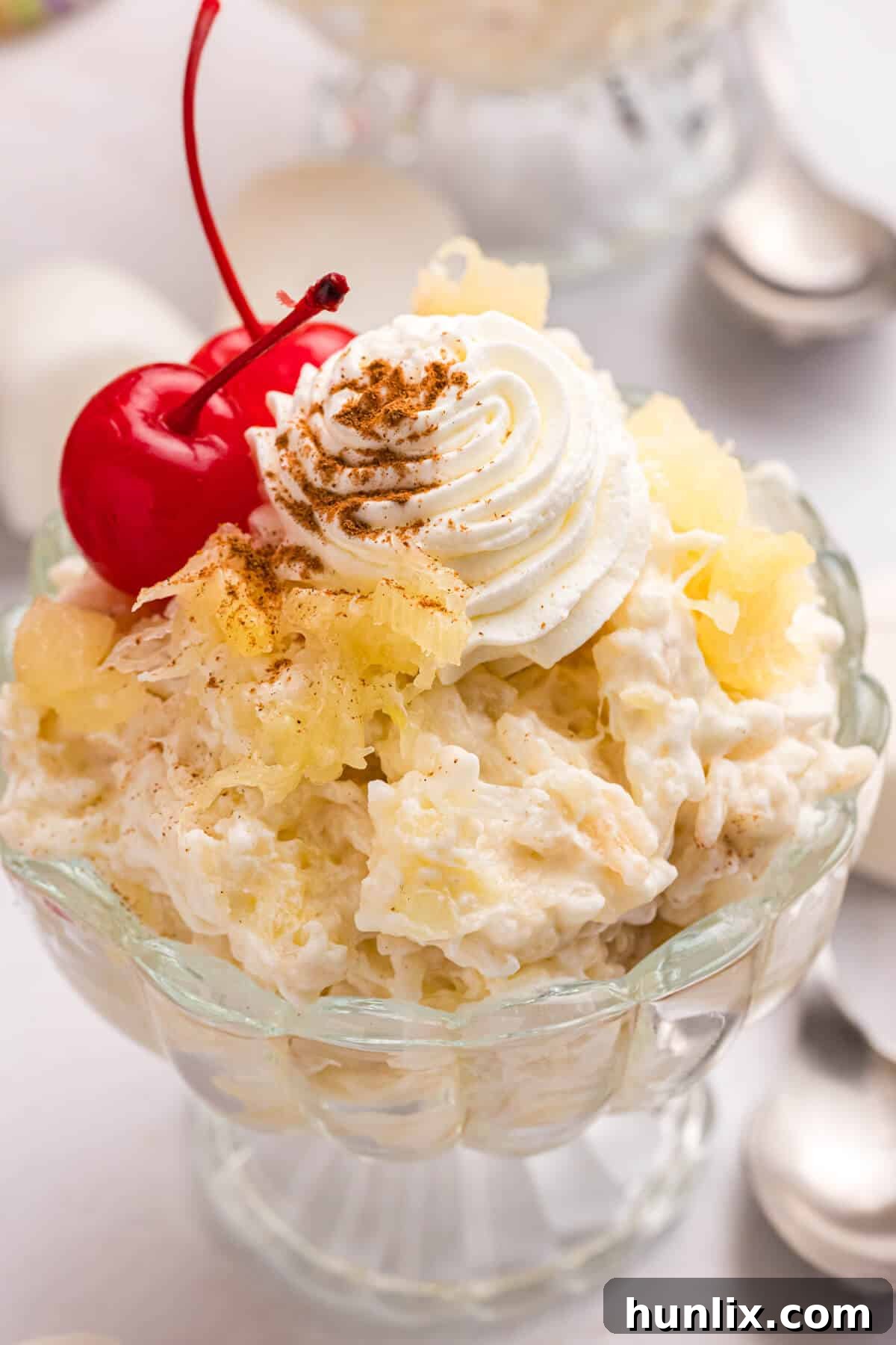 A serving of pineapple rice pudding in a glass bowl, garnished with a cherry.