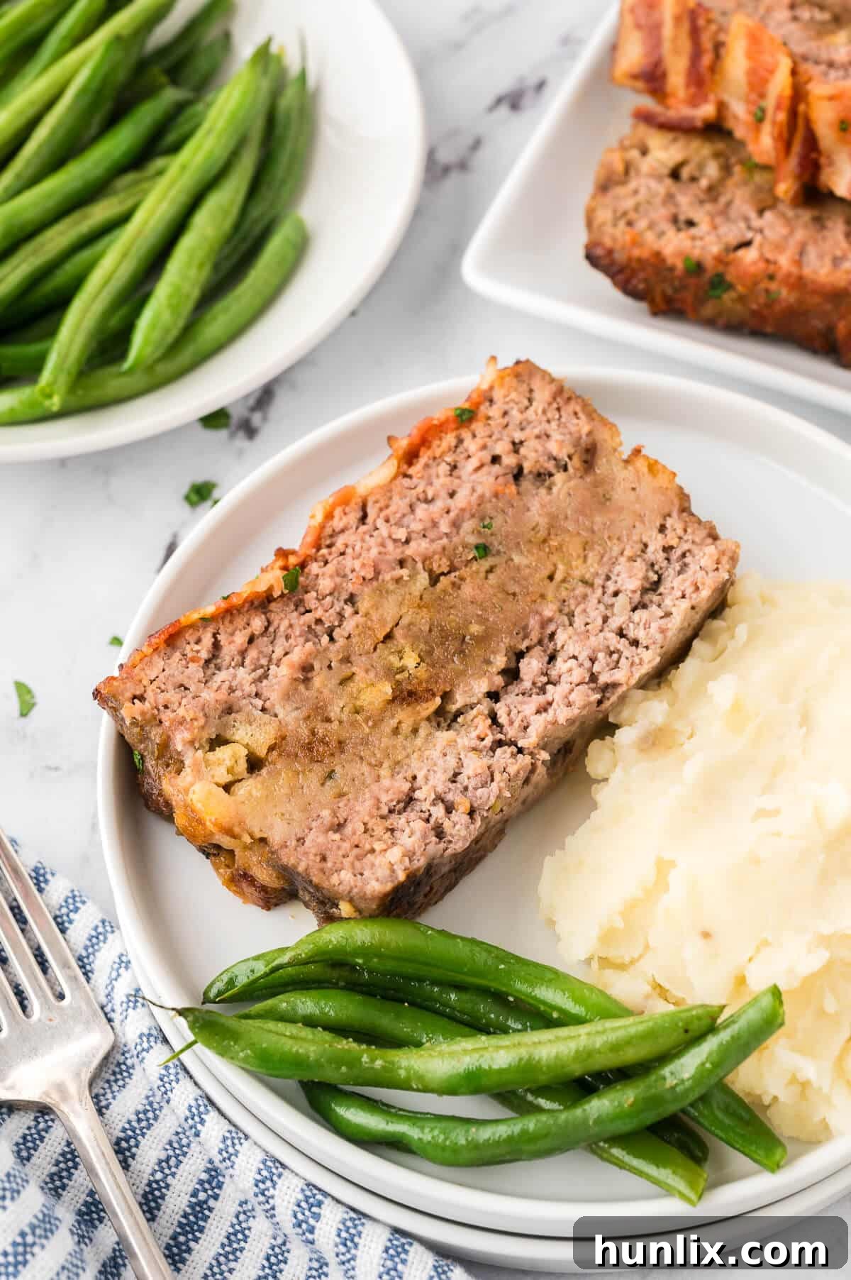 Sunday's Best Meatloaf 8 A slice of Sunday meatloaf on a white plate, served with a side of green beans and mashed potatoes.