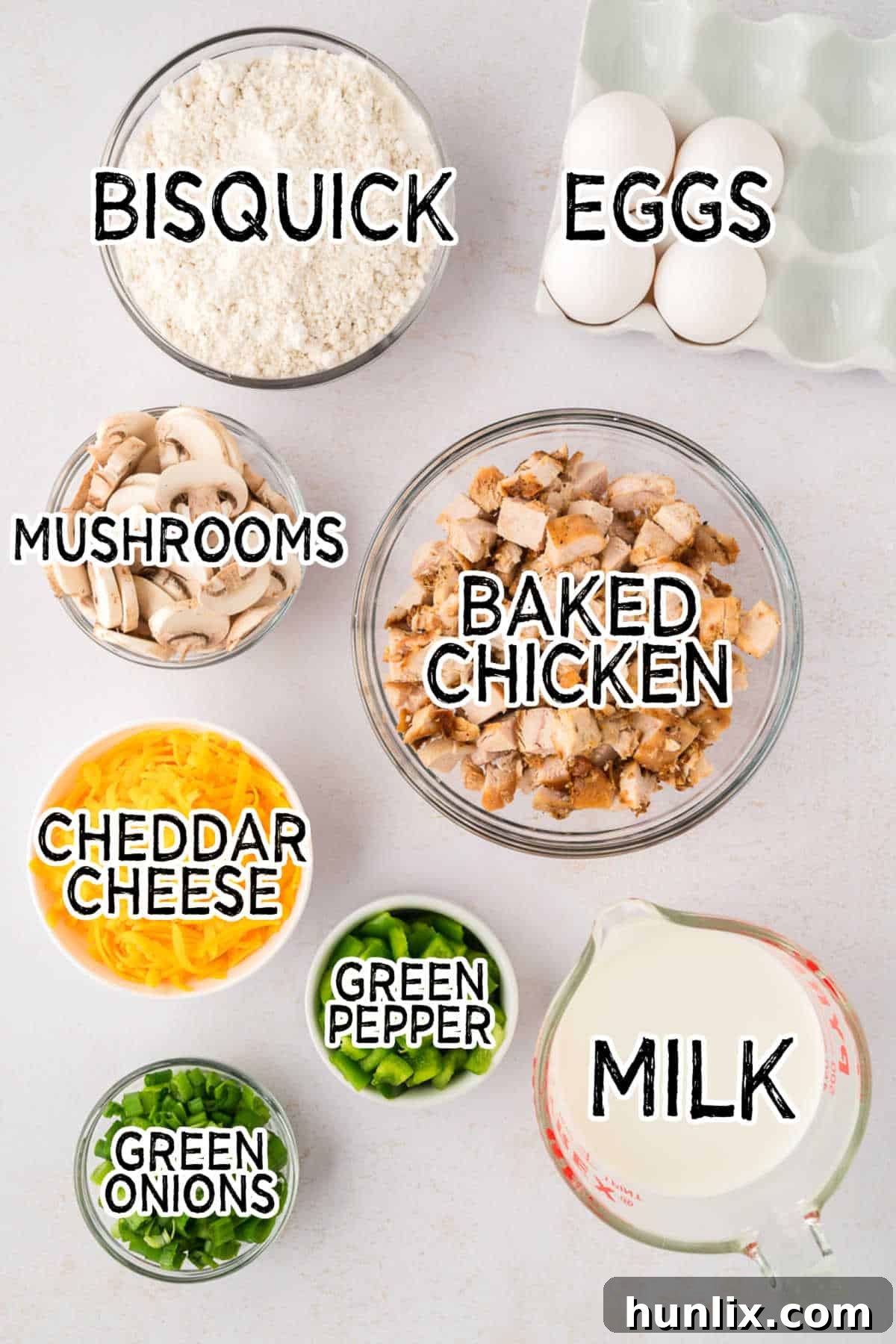 Effortless Chicken Pie 3 A collection of fresh ingredients laid out on a counter, including chicken, sliced mushrooms, green onions, green bell pepper, shredded cheddar cheese, milk, and a box of Bisquick, ready for making Impossible Chicken Pie.
