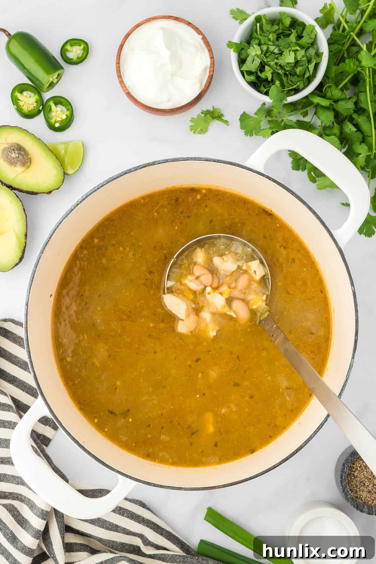 A steaming pot of White Chicken Chili with a ladle, ready to be served, highlighting its comforting warmth and rich texture.
