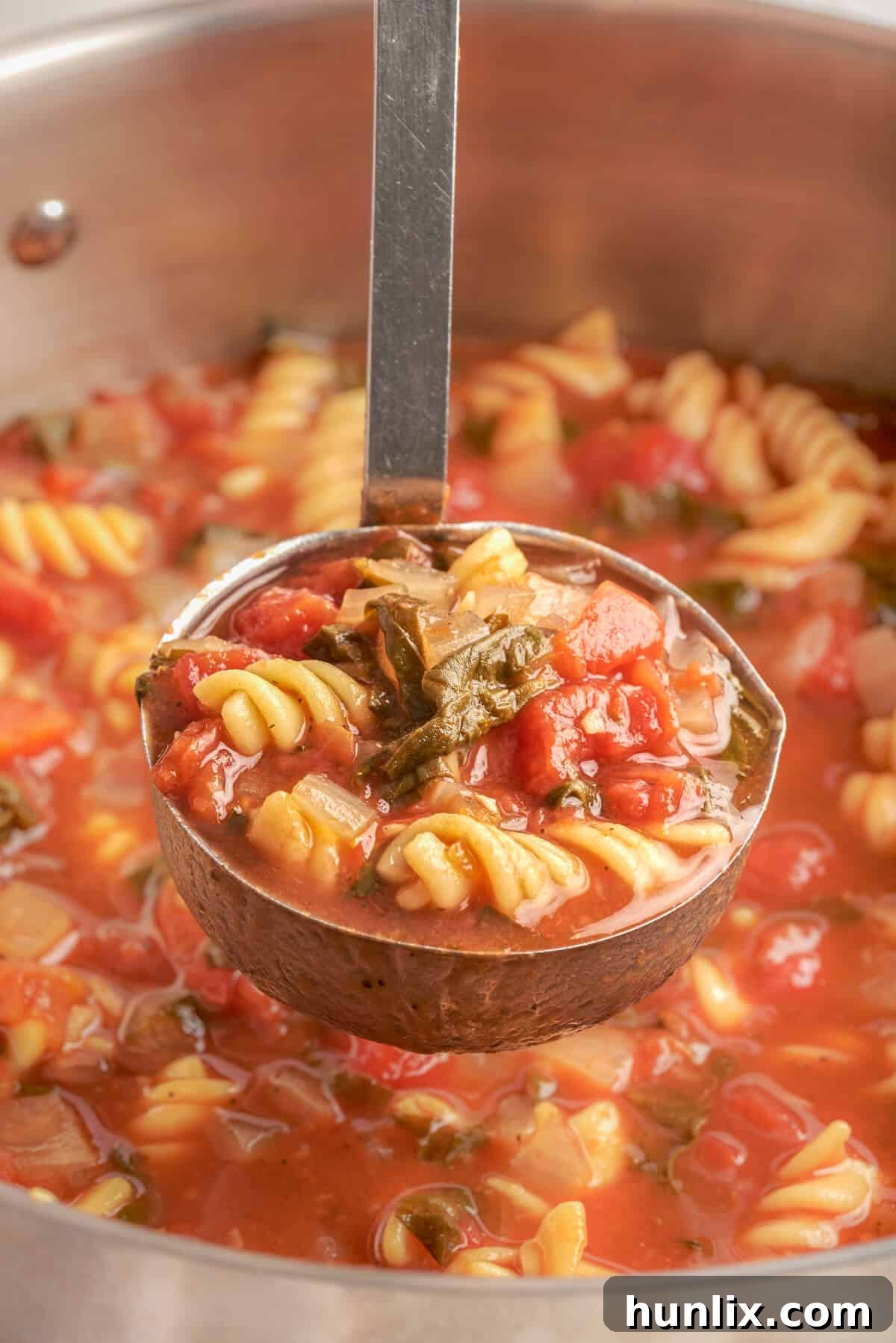 A soup ladle filled with creamy Tomato Florentine Soup, ready to be served.