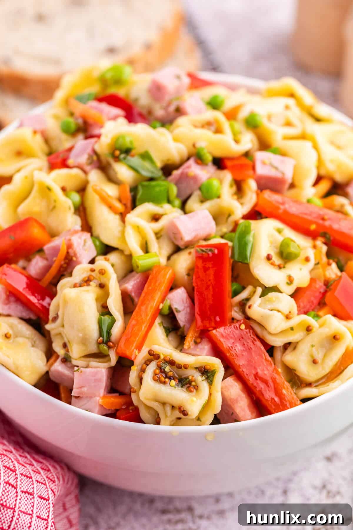 A large serving of tortellini salad in a white bowl, glistening with dressing.