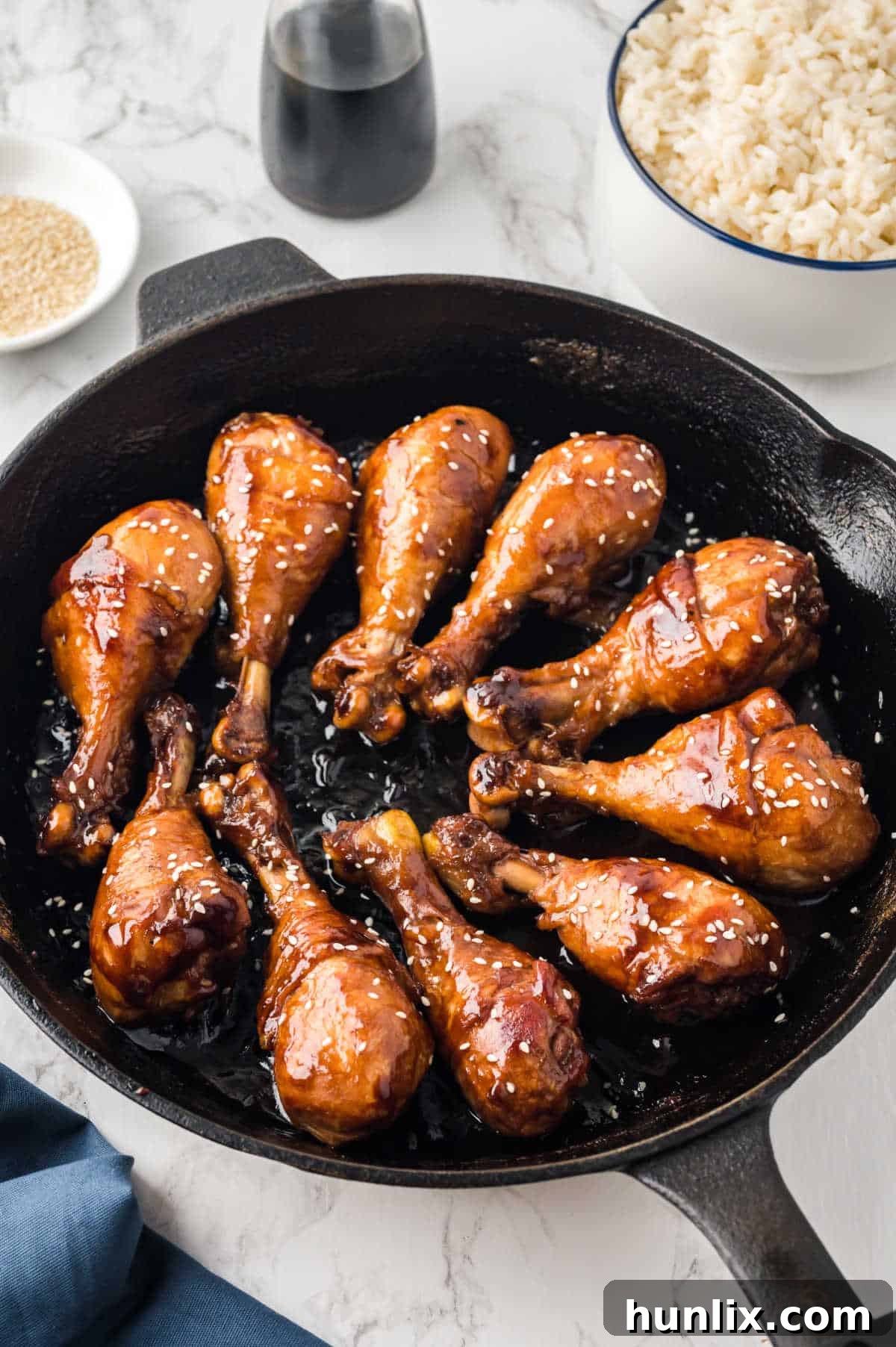 Sticky chicken drumsticks in a cast iron skillet, garnished with sesame seeds.