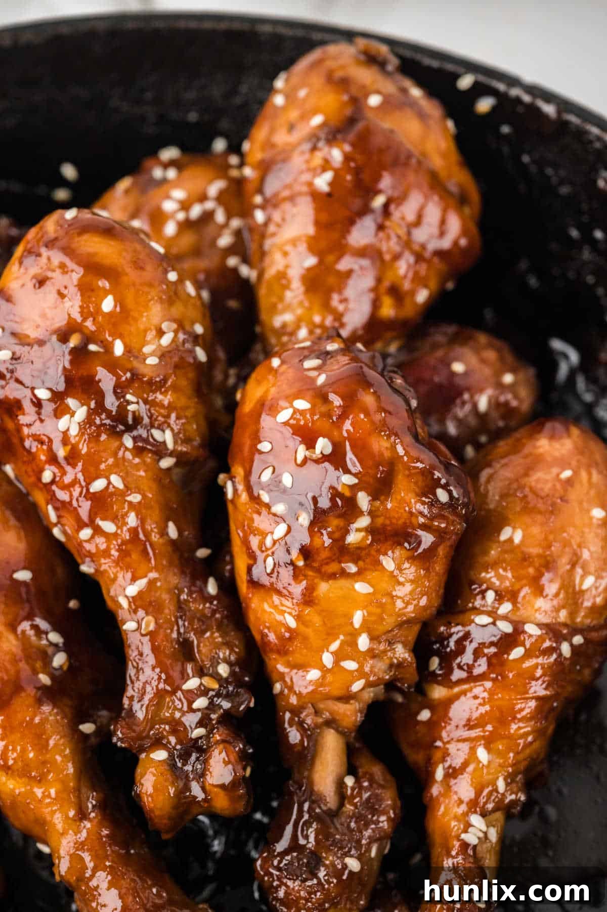 Close-up of golden brown chicken drumsticks simmering in the sticky sauce in a pan.