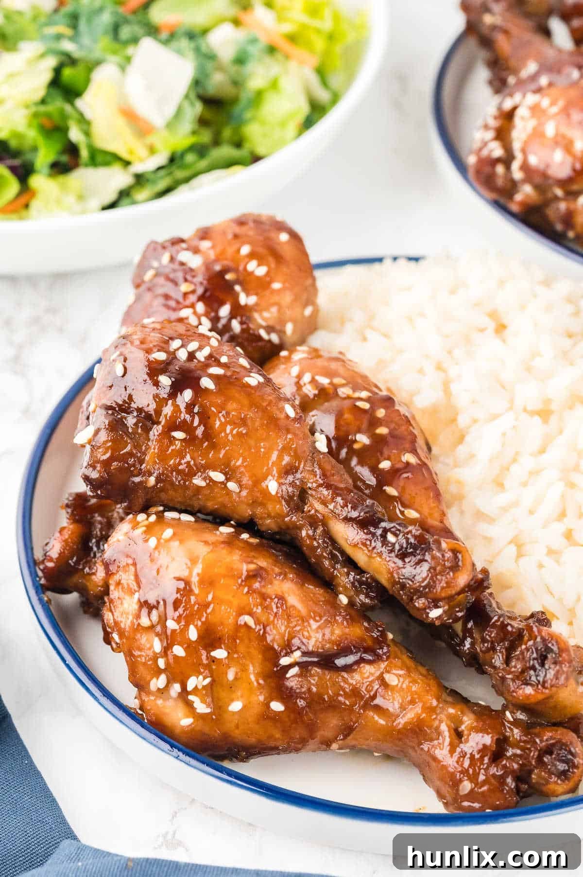 A serving of sticky chicken with white rice on a plate, garnished with sesame seeds.