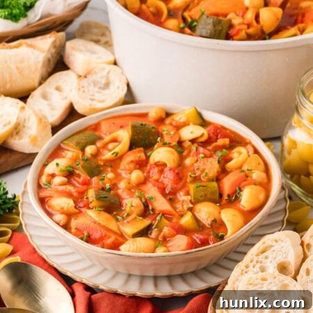 A vibrant bowl of Minestrone Soup, ready to be served, garnished with fresh herbs and a drizzle of olive oil.