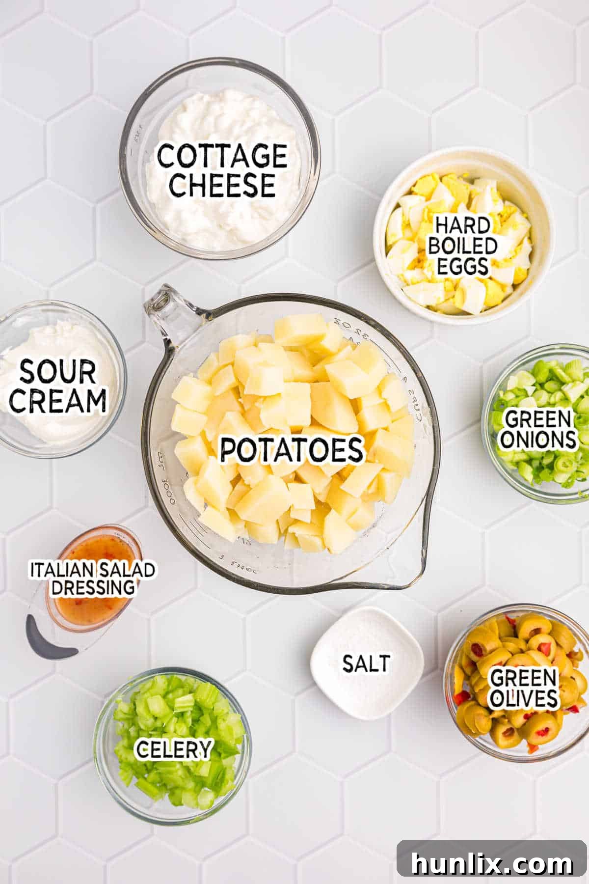 A neatly arranged display of fresh ingredients for cheese potato salad, including potatoes, eggs, celery, olives, and cottage cheese.