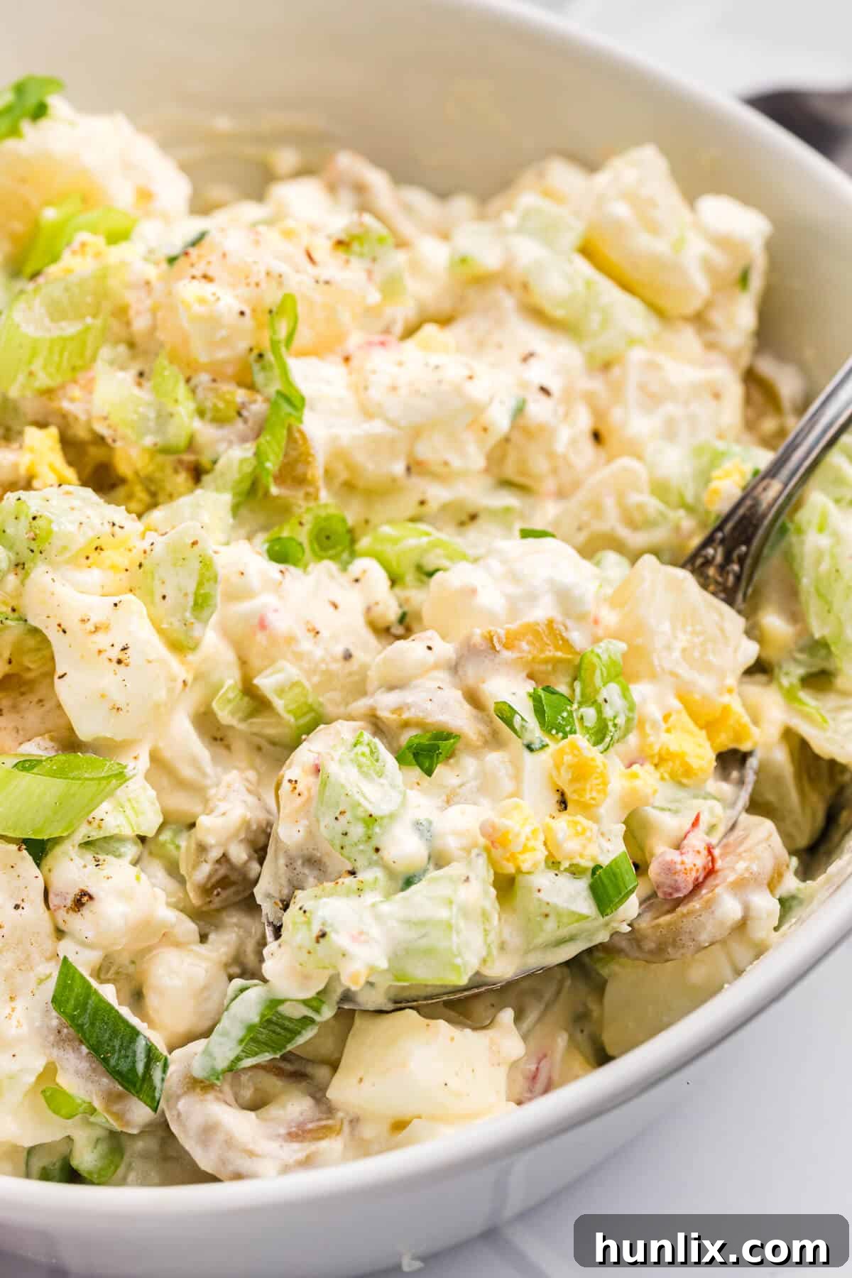 A close-up shot of cheese potato salad with a serving spoon, highlighting its creamy texture and visible ingredients.