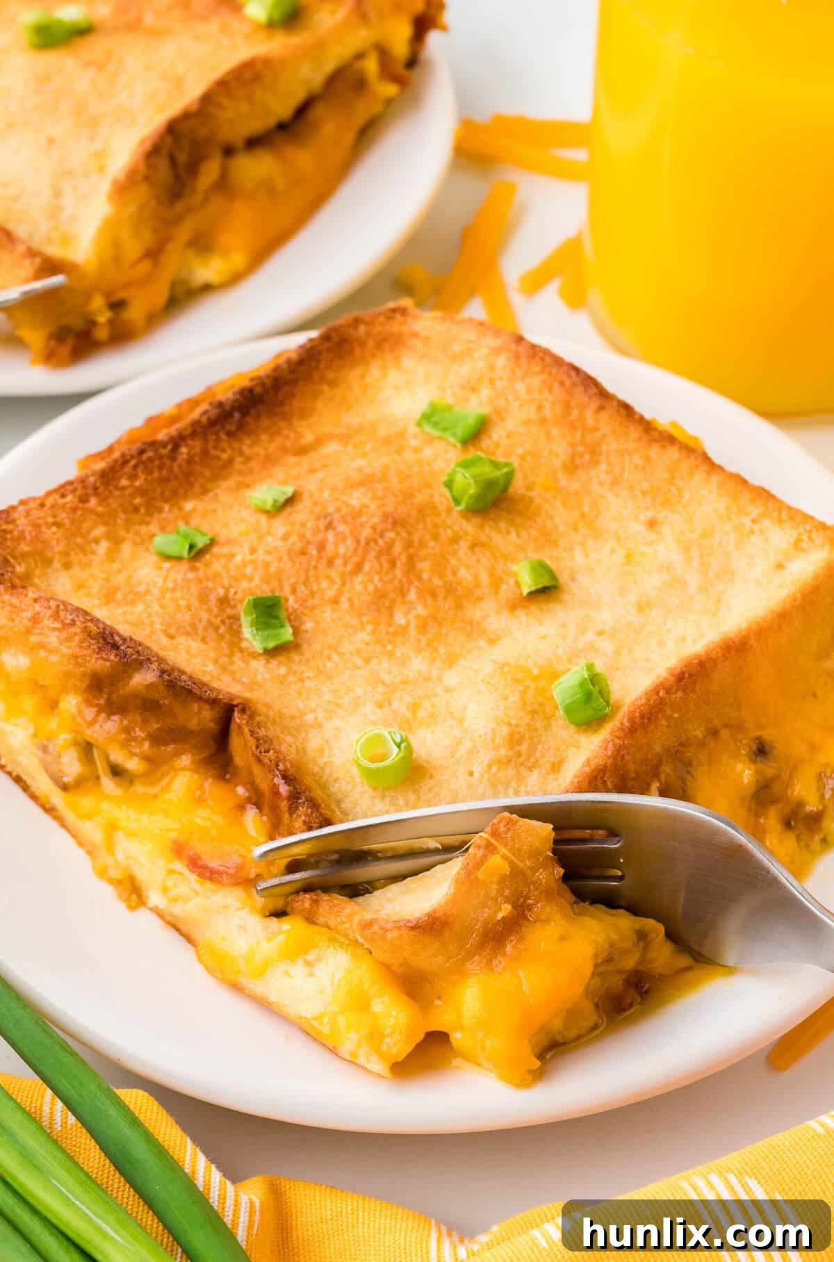 A delicious piece of bacon breakfast casserole on a white plate, accompanied by a silver fork, ready to be enjoyed.
