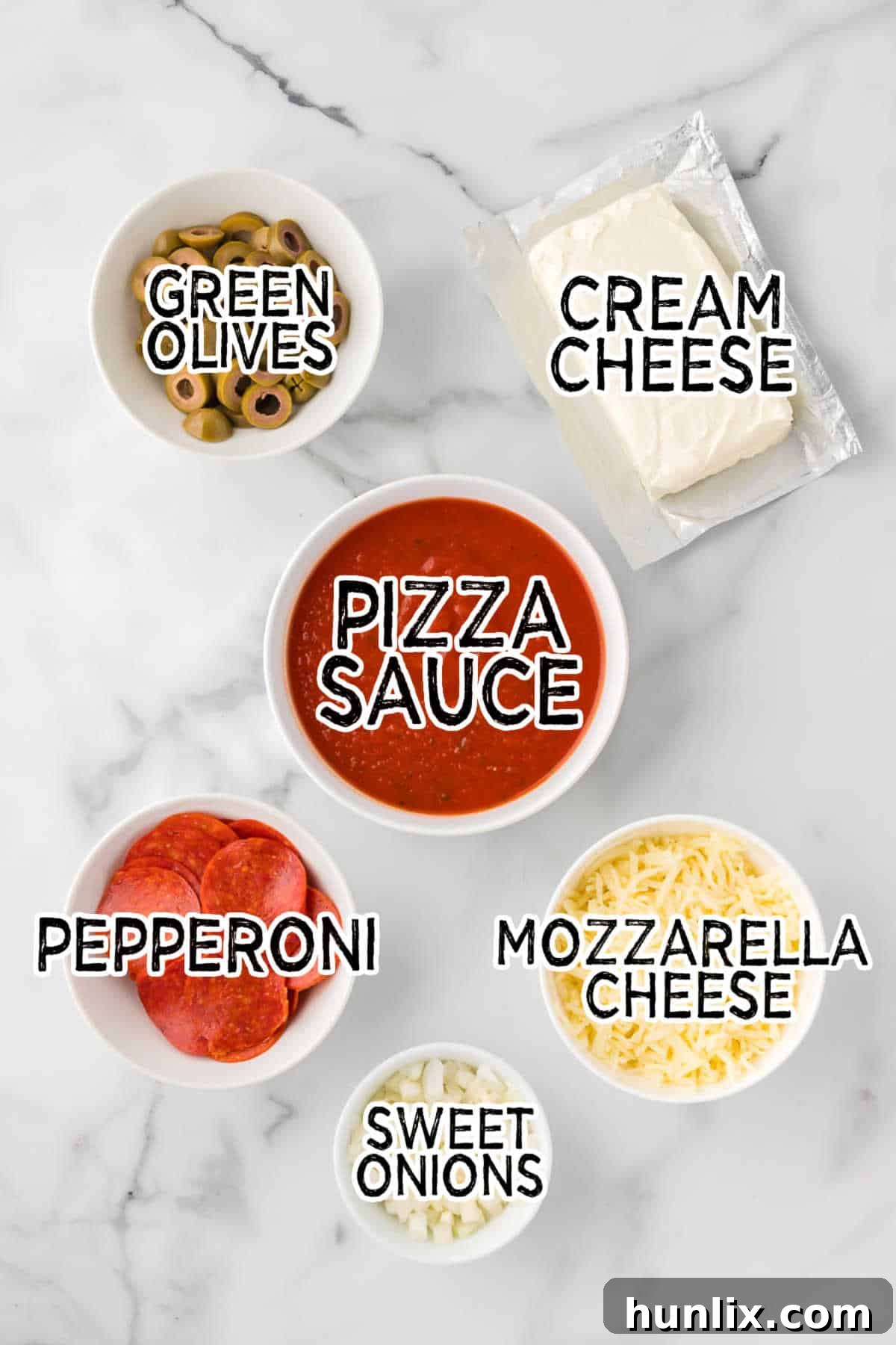 All the fresh ingredients for pizza dip – cream cheese, pizza sauce, mozzarella, green olives, pepperoni, and sweet onions – neatly arranged on a clean white marble counter.