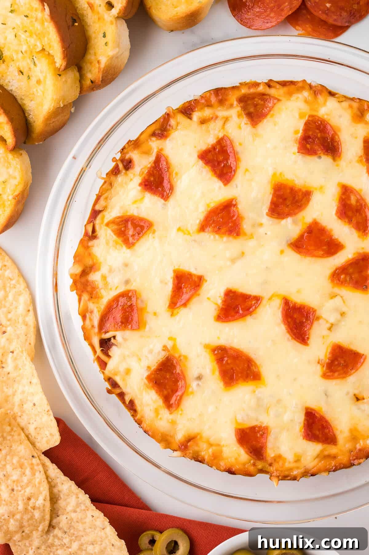 A delicious pizza dip in a pie pan, surrounded by freshly baked garlic bread and various chips, prepared for a delightful party spread.