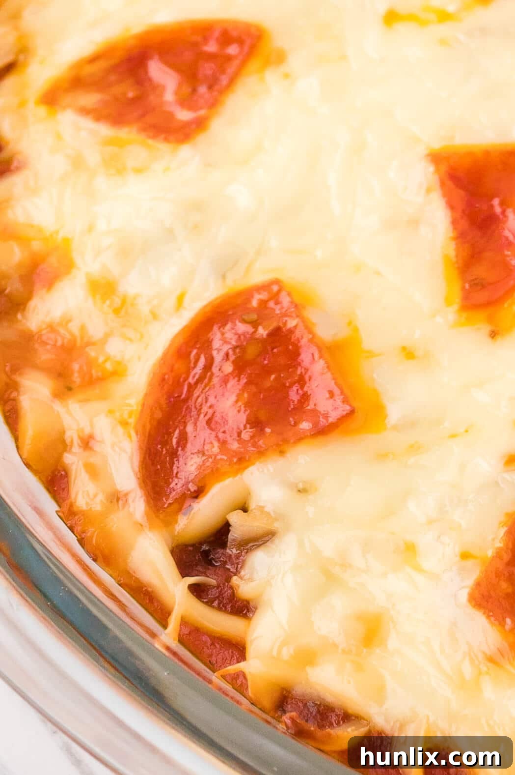 A close-up shot of the hot, bubbly pizza dip, showing perfectly melted mozzarella cheese, visible pepperoni, and green olives, inviting a taste.