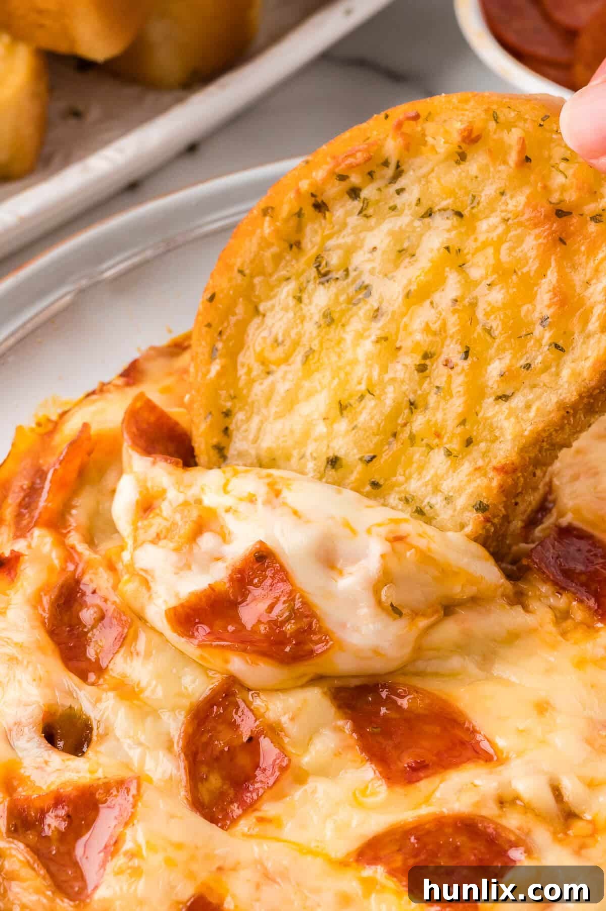 A hand dipping a piece of golden, crispy garlic bread into the warm, cheesy pizza dip, creating a delicious moment.