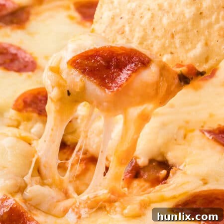 A crispy tortilla chip being expertly dipped into a hot and cheesy pizza dip, showcasing its melted goodness.