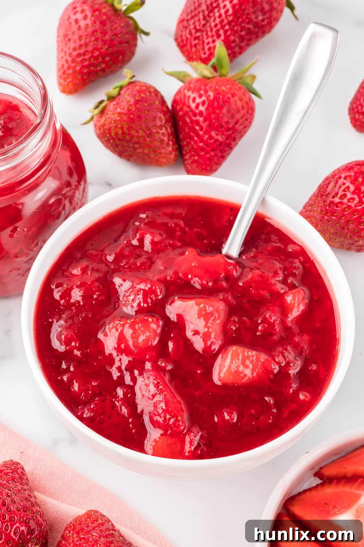 A bowl filled with rich, red strawberry sauce, accompanied by a spoon ready for tasting.