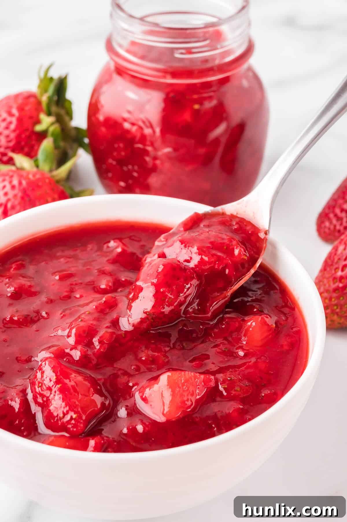 Another view of a bowl of strawberry sauce with a spoon, highlighting its thick and inviting texture.