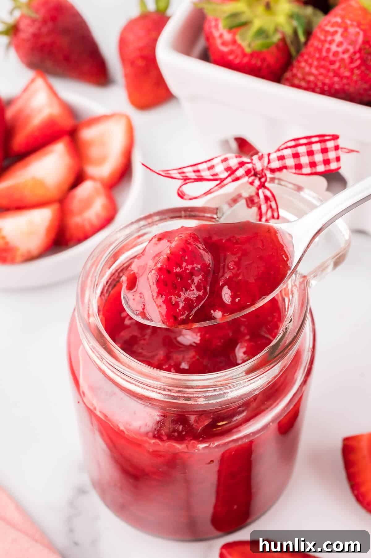 A jar of strawberry sauce with a spoon resting inside, hinting at its homemade goodness.