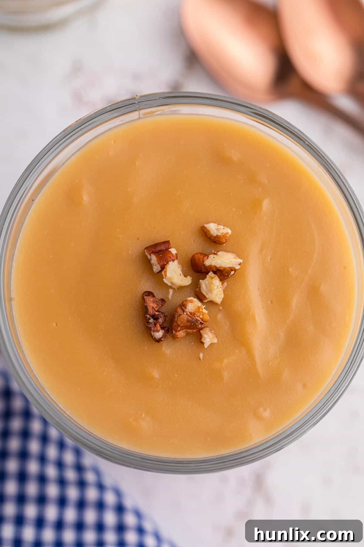 Silky Butterscotch Indulgence 7 A decadent serving of homemade butterscotch pudding, elegantly topped with crunchy pecans, presented in a clear glass parfait dish.