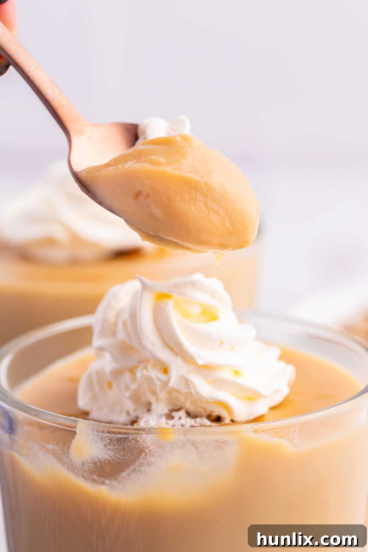 Silky Butterscotch Indulgence 8 A close-up shot of a spoon scooping a generous portion of creamy butterscotch pudding from a clear parfait dish, highlighting its smooth texture.