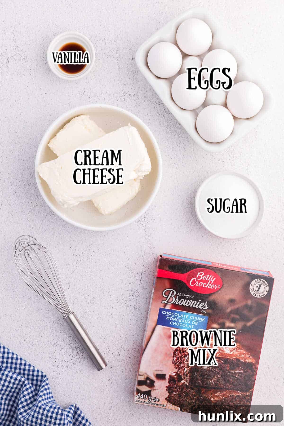 Five ingredients laid out for brownie bottom cheesecake: brownie mix, cream cheese, eggs, sugar, and vanilla extract.