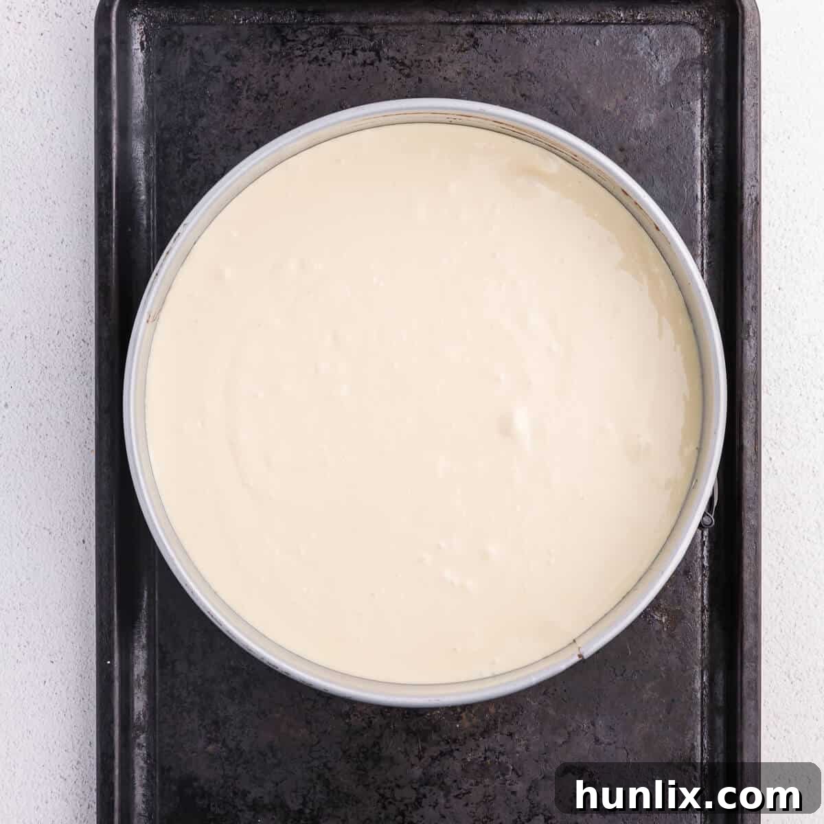 Creamy cheesecake filling spread over the baked brownie layer in a springform pan, ready for the oven.