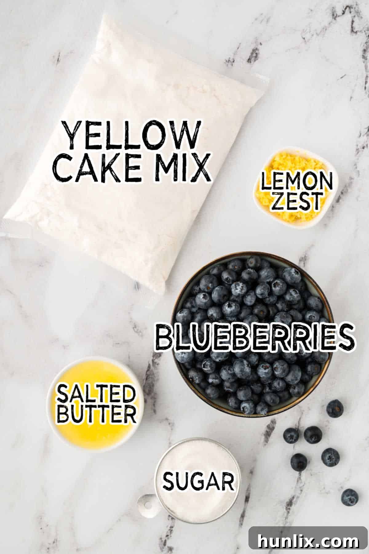 Inverted Blueberry Bliss 3 A flat lay photograph showcasing the simple ingredients for blueberry upside down cake: butter, sugar, fresh blueberries, and lemons on a white marble background.
