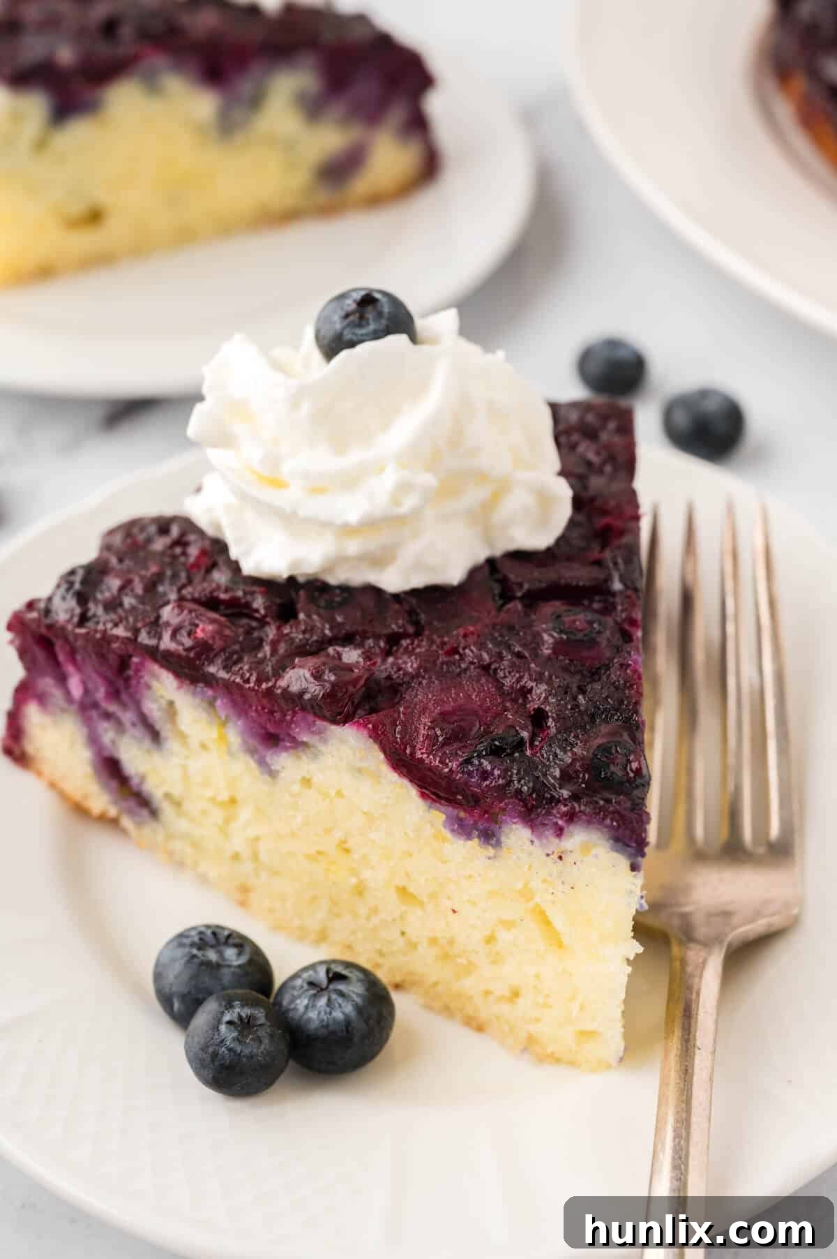 Inverted Blueberry Bliss 8 A slice of blueberry upside down cake on a plate with a fork, showing the moist cake and fruit topping.