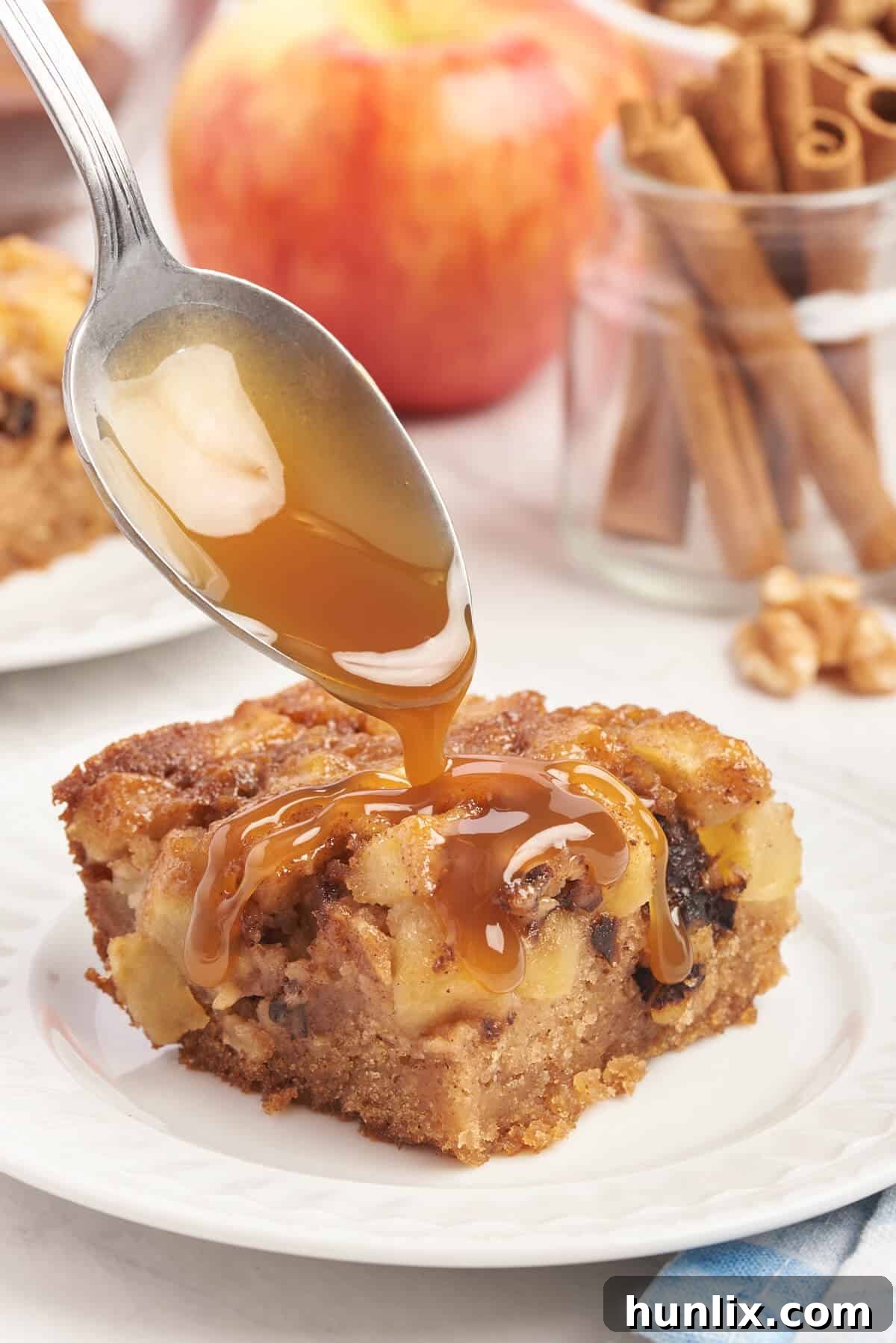 A close-up shot of a spoon drizzling rich caramel sauce over a slice of Nobby Apple Cake.