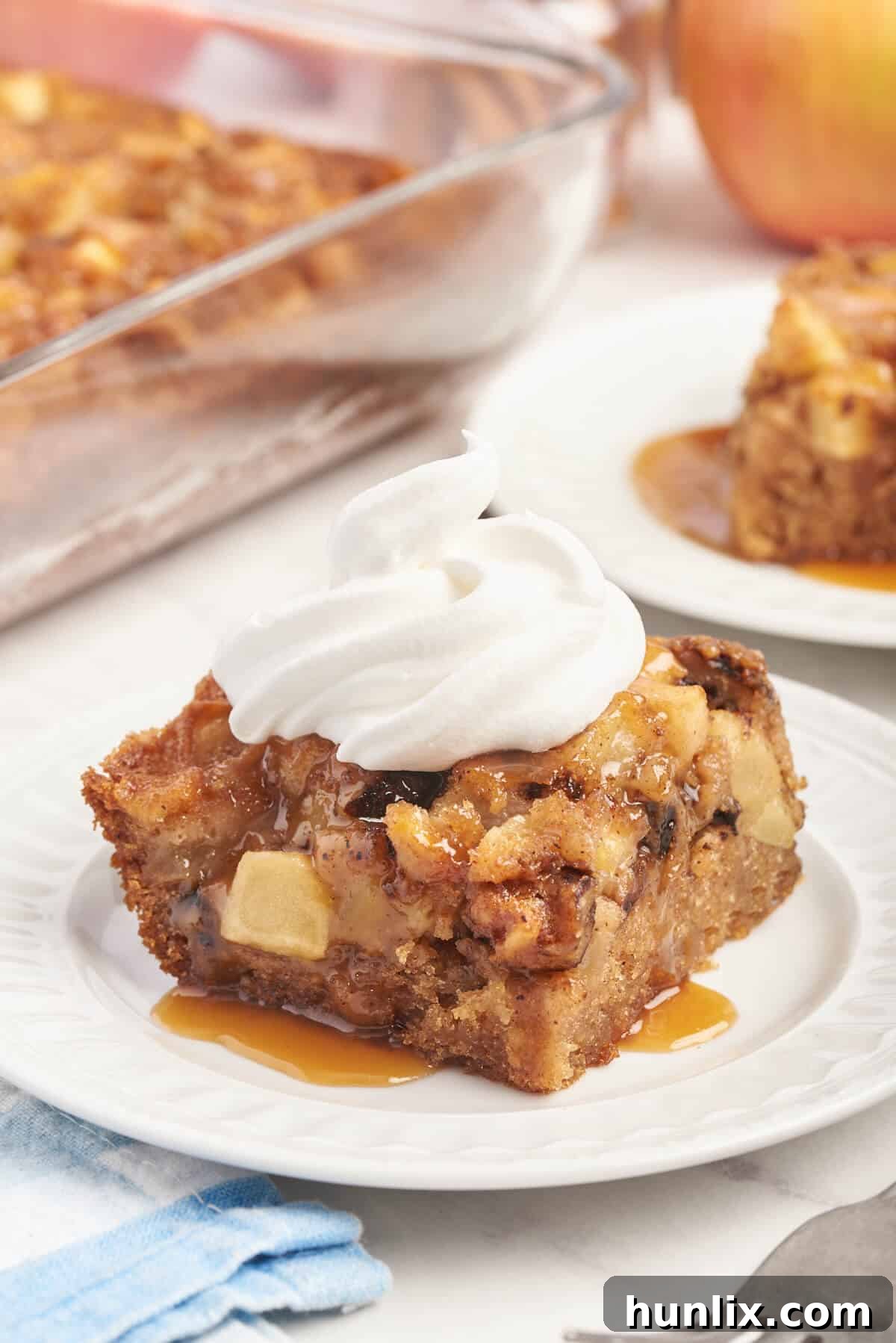 A delectable piece of Nobby Apple Cake artfully arranged on a plate, crowned with a generous swirl of whipped cream.