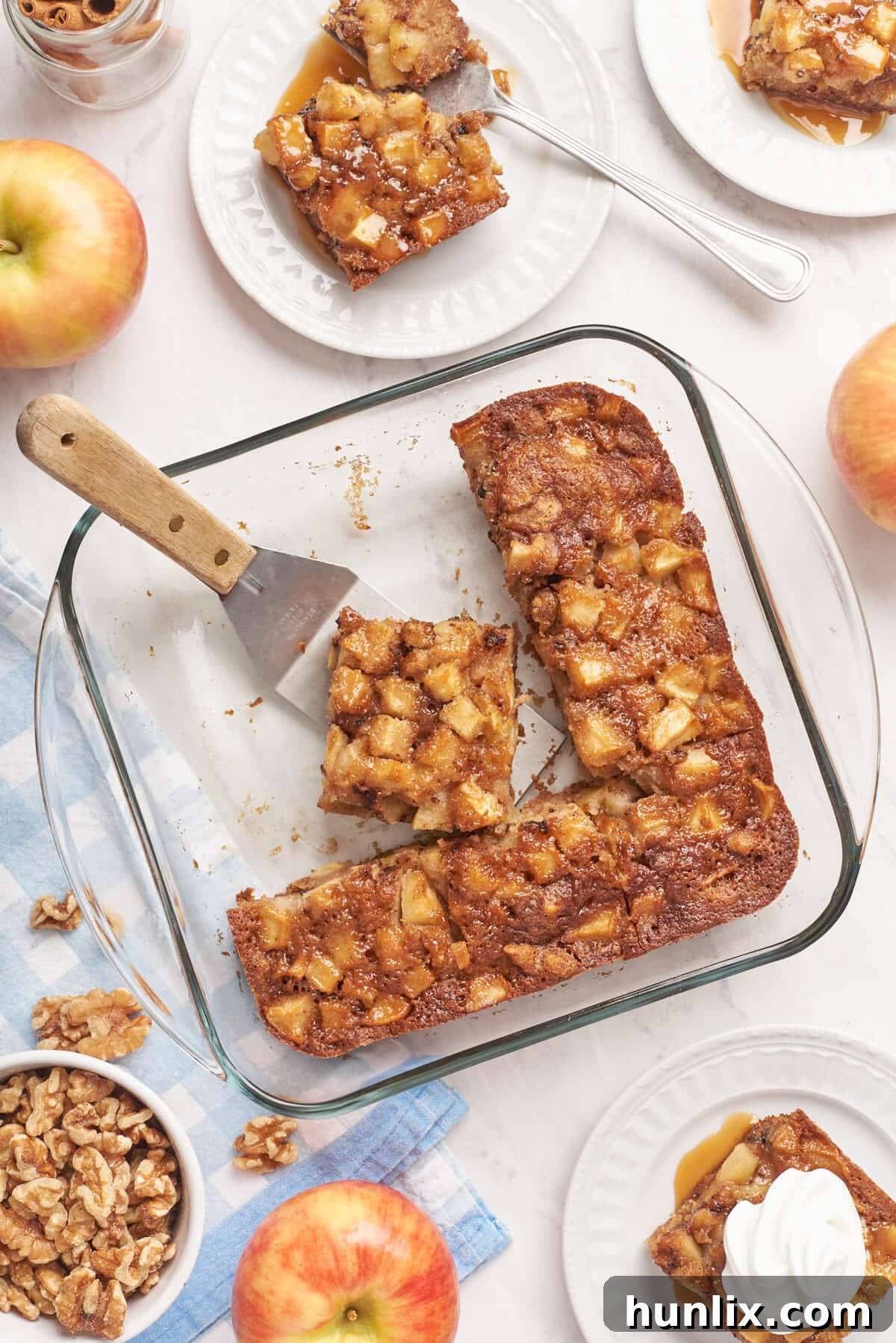 A close-up view of a square Nobby Apple Cake in its pan, with several slices already removed, revealing the moist interior.