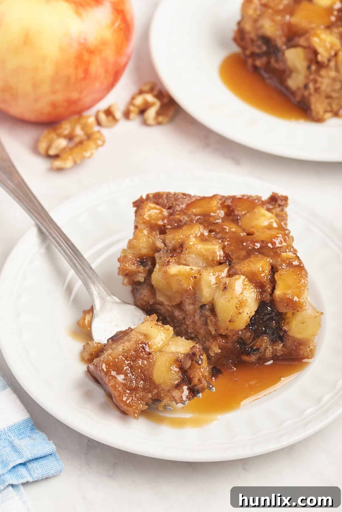 A slice of Nobby Apple Cake on a white plate, accompanied by a fork, ready to be enjoyed.