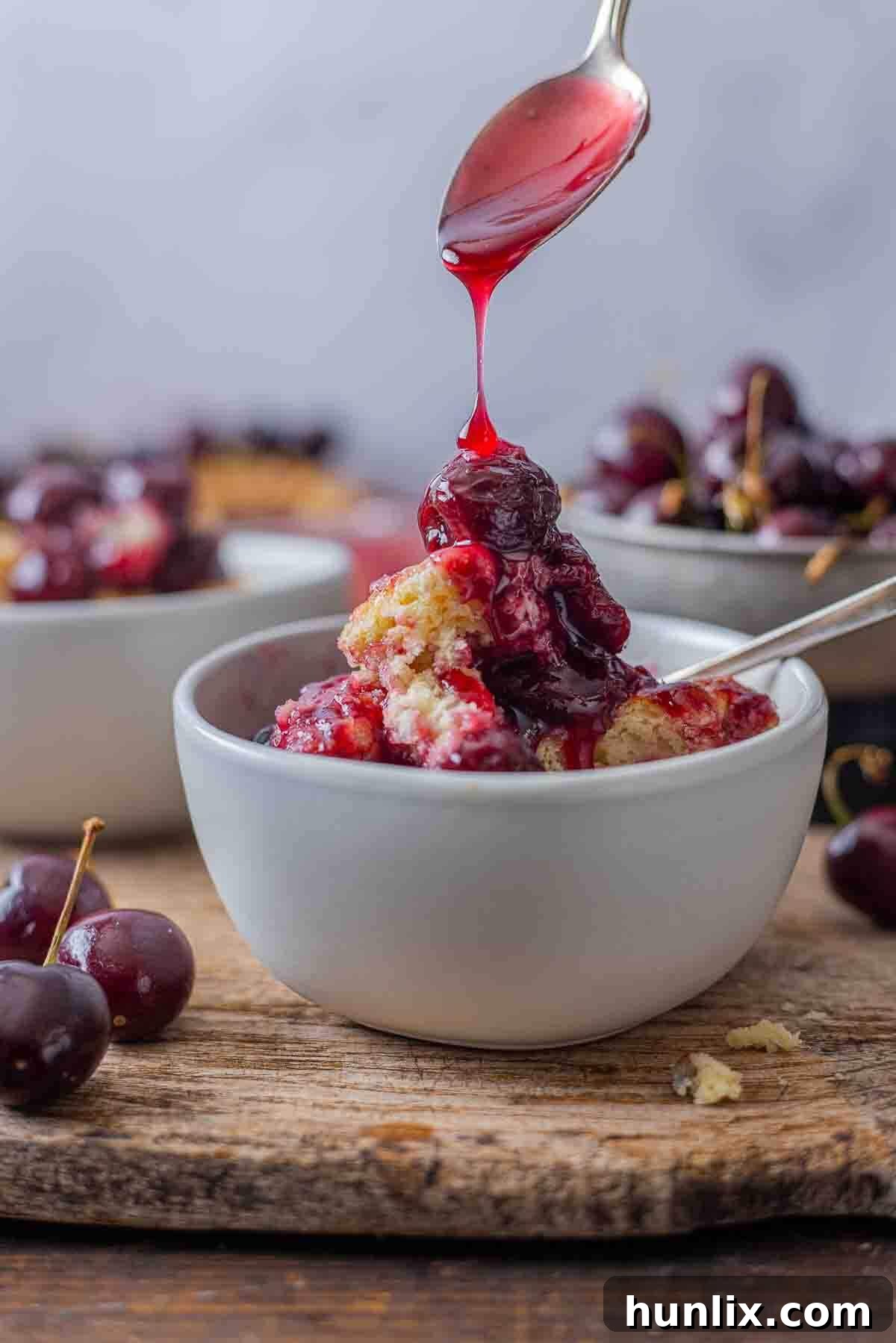 Fireside Cherry Cobbler 7 A spoon drizzling cherry sauce on the recipe in a bowl.