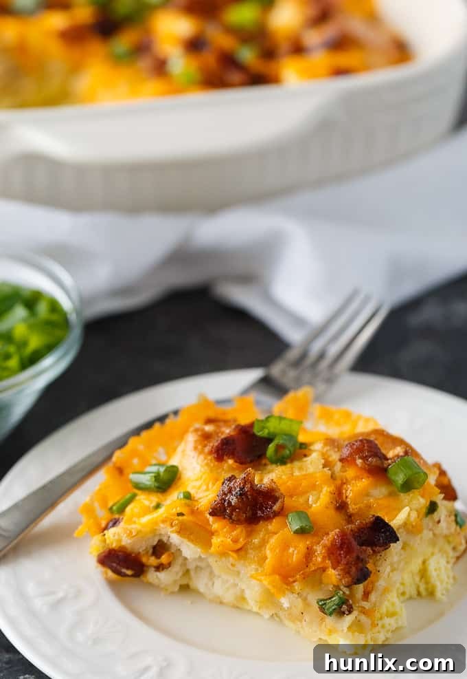 A serving of Bacon and Egg Biscuit Casserole in a square dish, with a fork ready to enjoy.