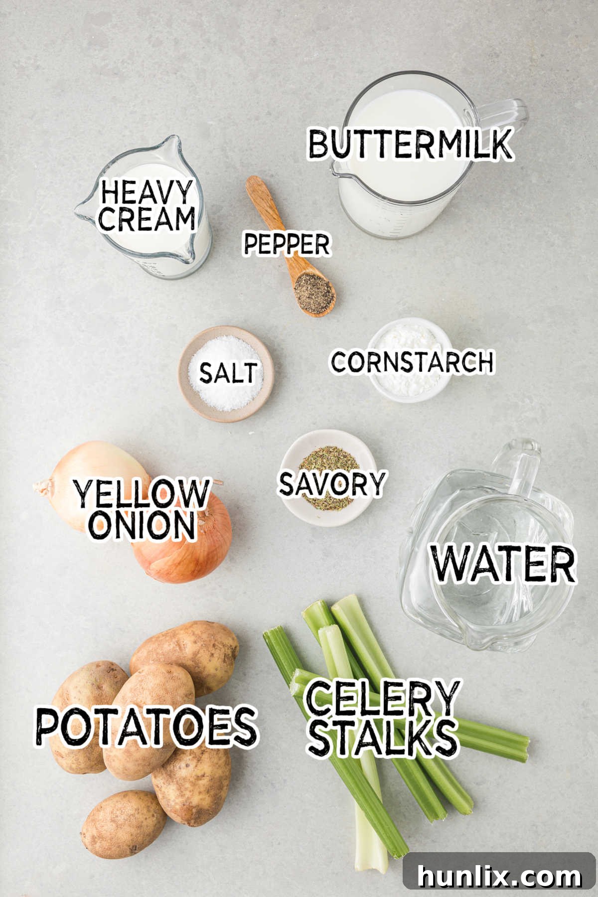 Fresh ingredients laid out on a gray surface, including potatoes, onion, celery, and herbs, ready for German potato soup preparation.