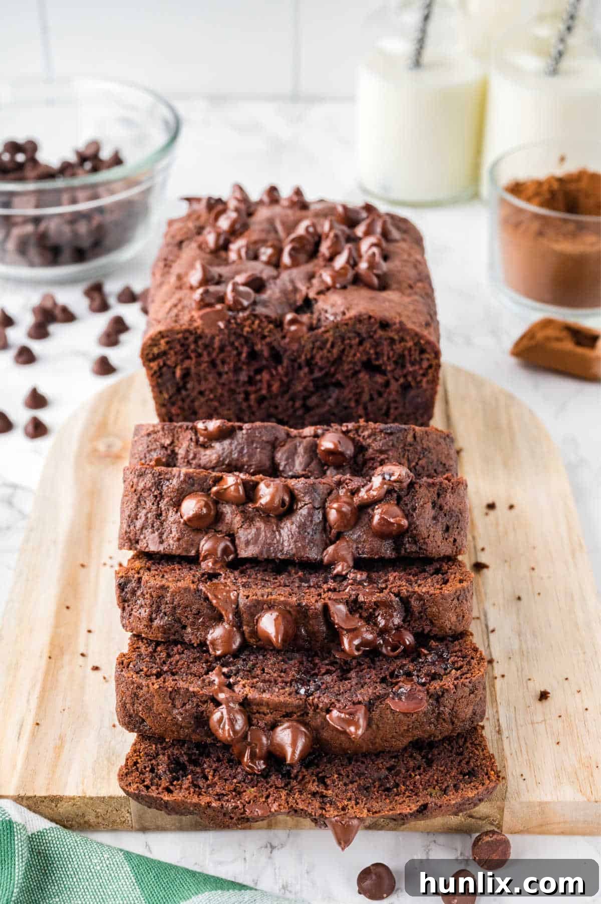 A loaf of chocolate zucchini bread partially cut into slices on a wooden cutting board.