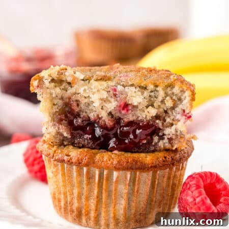 A stack of banana raspberry muffins on a plate, with a bite taken from the top one, revealing the jam center.