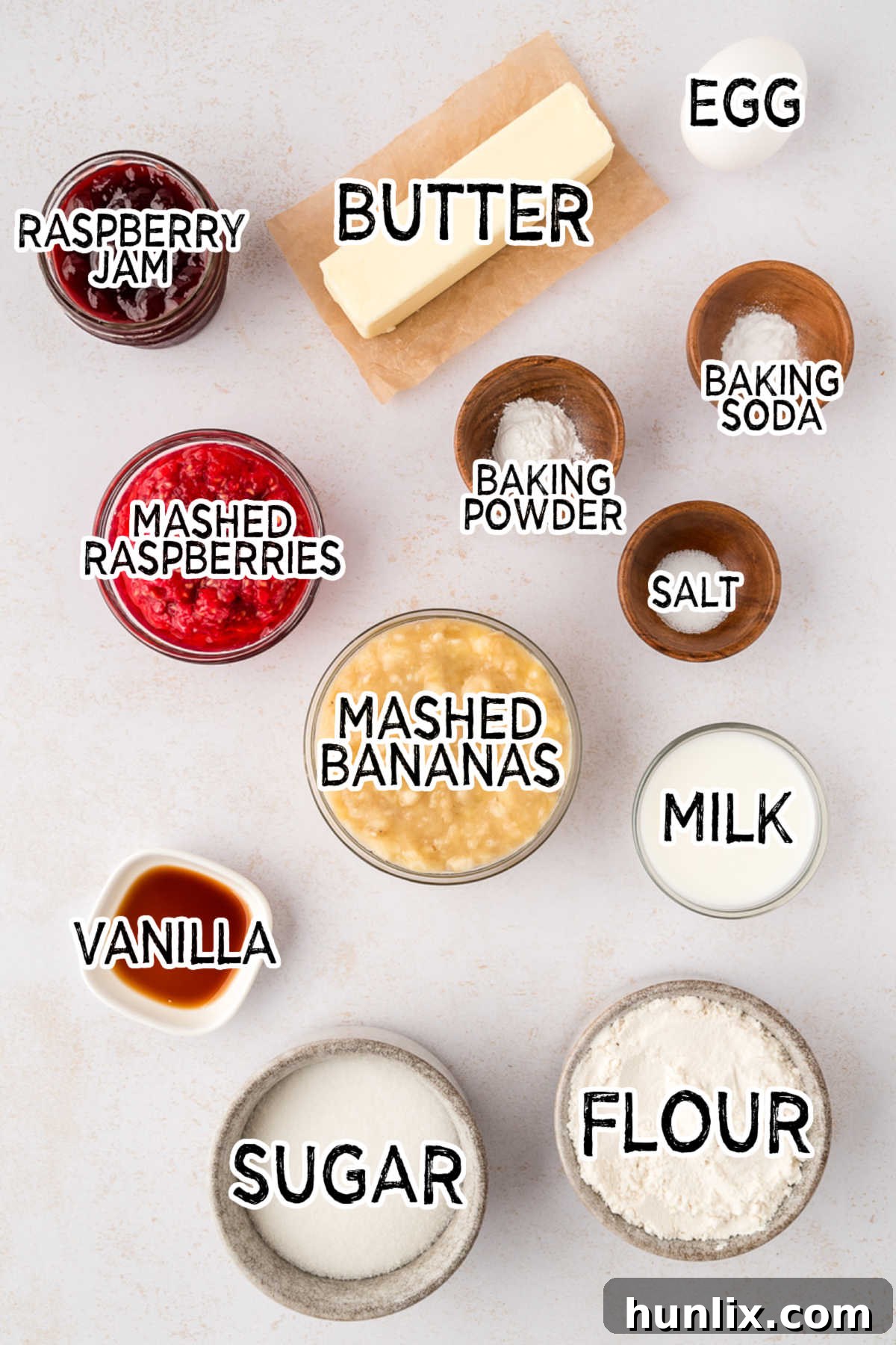 Golden Banana Raspberry Bliss Muffins 3 All the ingredients for Banana Raspberry Muffins laid out on a white surface, including flour, sugar, butter, eggs, bananas, raspberries, milk, and jam.