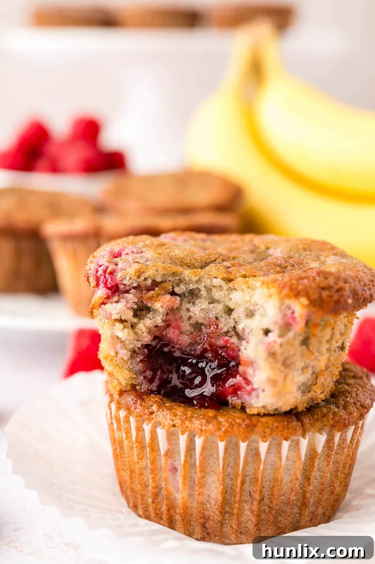 Golden Banana Raspberry Bliss Muffins 8 A perfectly arranged stack of three Banana Raspberry Muffins on a white plate, showcasing their fluffy texture and golden-brown tops.