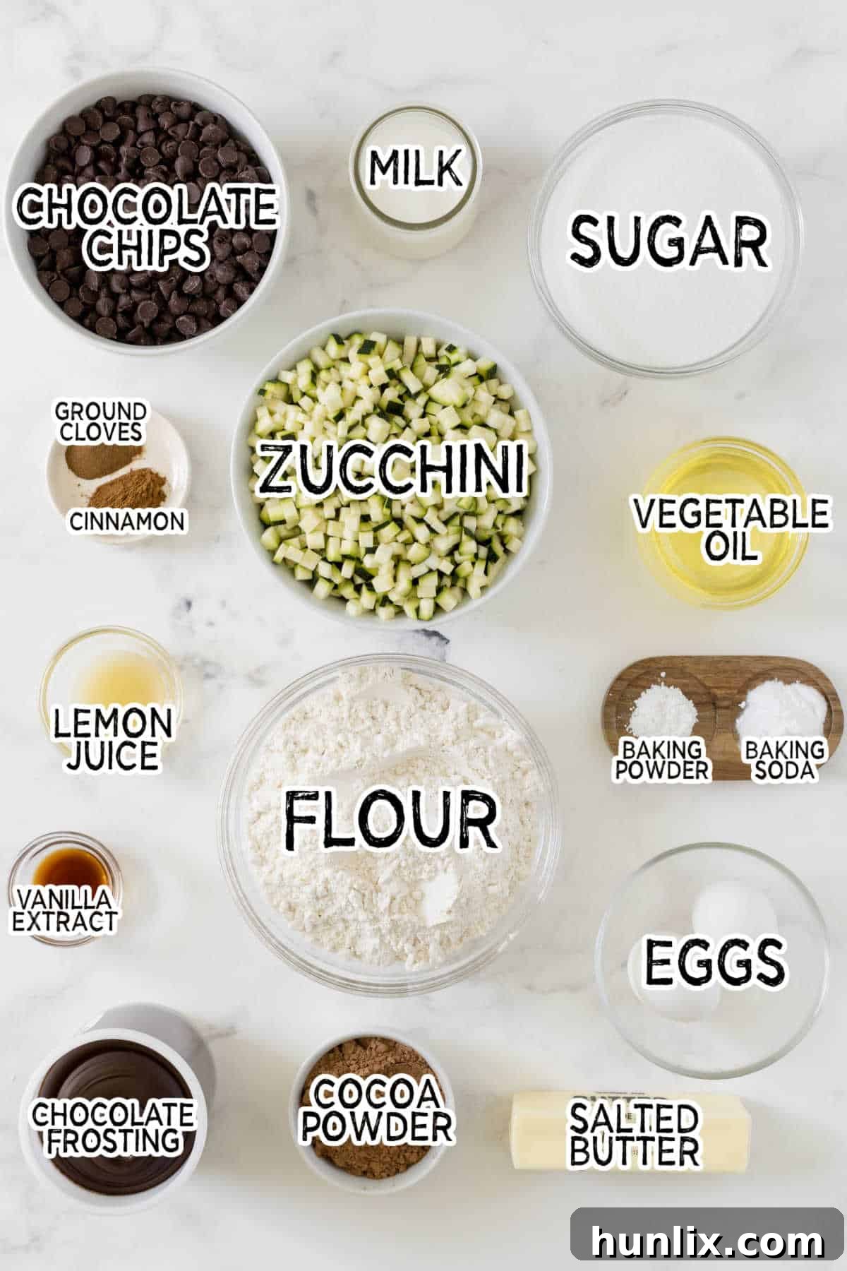 All the fresh ingredients for Chocolate Zucchini Cake laid out beautifully on a white marble background, including vibrant green zucchini, rich cocoa powder, farm-fresh eggs, creamy butter, and decadent chocolate chips.