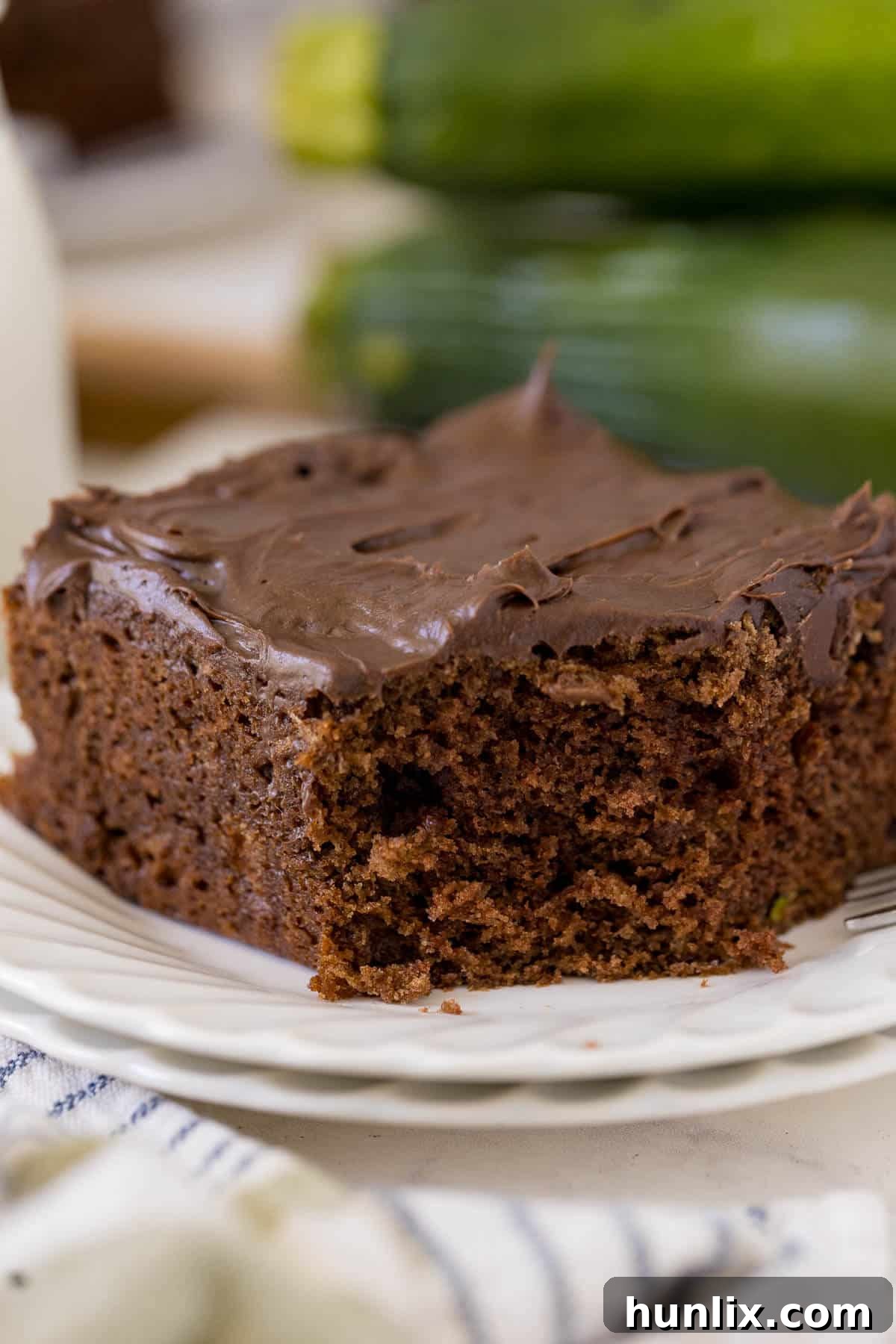A delectable slice of chocolate zucchini cake with a bite taken out of it, revealing its moist interior and tempting chocolate chips, served elegantly on a white plate.
