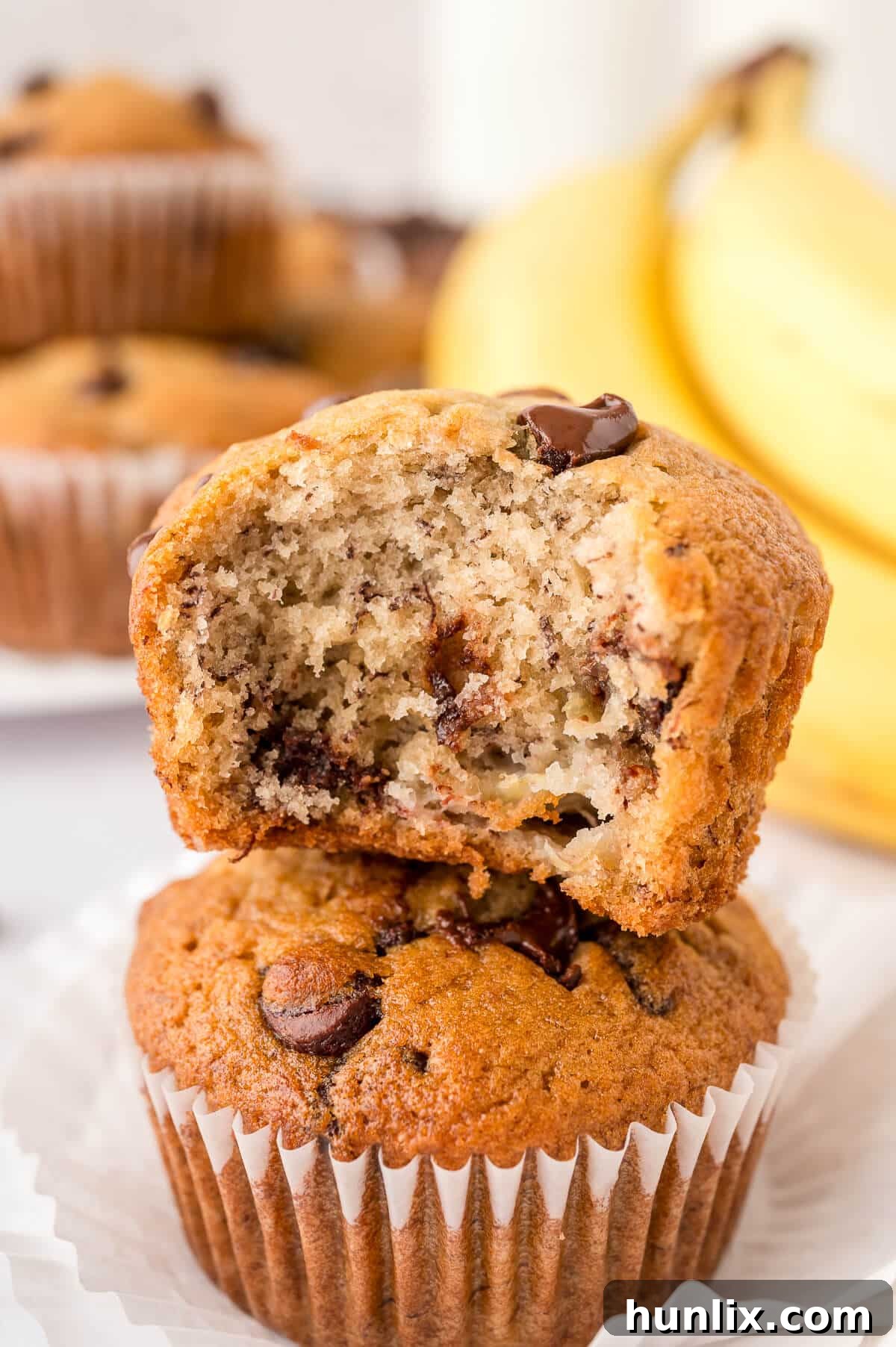 Decadent Banana Chocolate Chip Muffins 10 A stack of golden-brown banana chocolate chip muffins, with one muffin showing a delightful bite taken out of it.